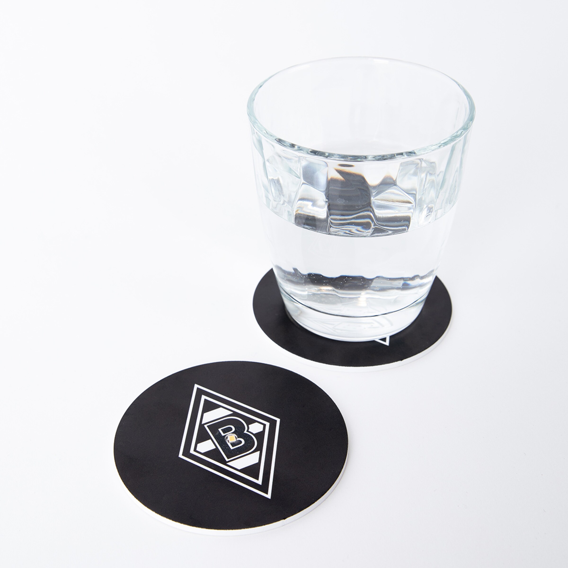 Ein Glas Wasser steht auf Untersetzern mit dem Borussia Mönchengladbach-Logo.