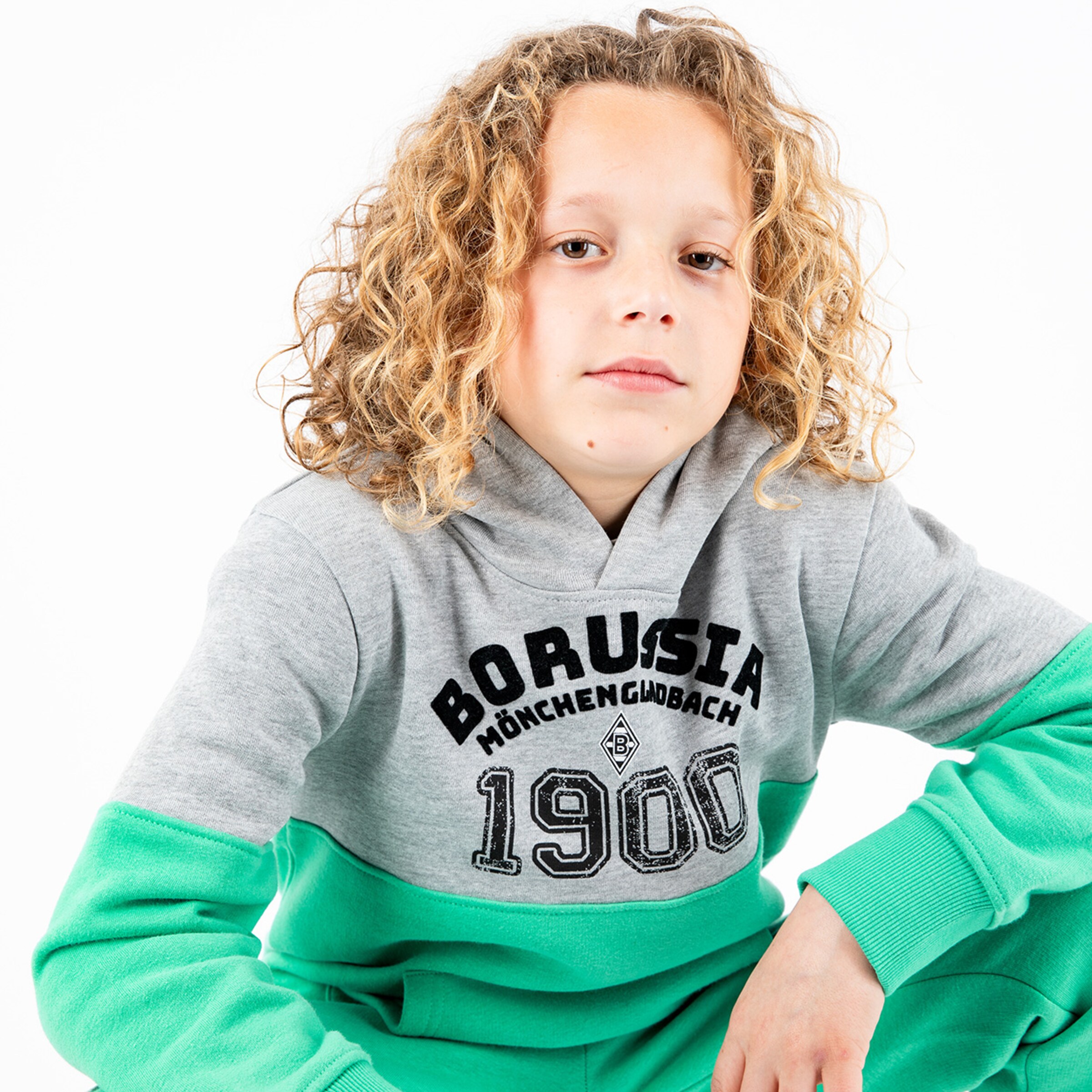 Junge mit lockigen Haaren trägt einen grauen und grünen Borussia Mönchengladbach Hoodie.