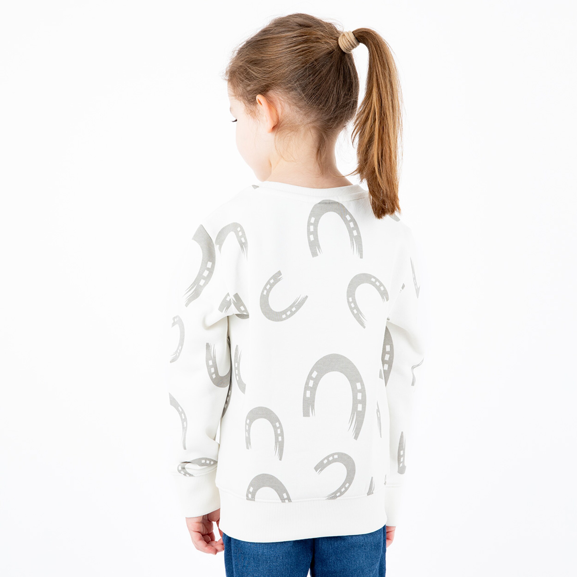 A girl wearing a white sweatshirt with a horseshoe pattern viewed from the back.