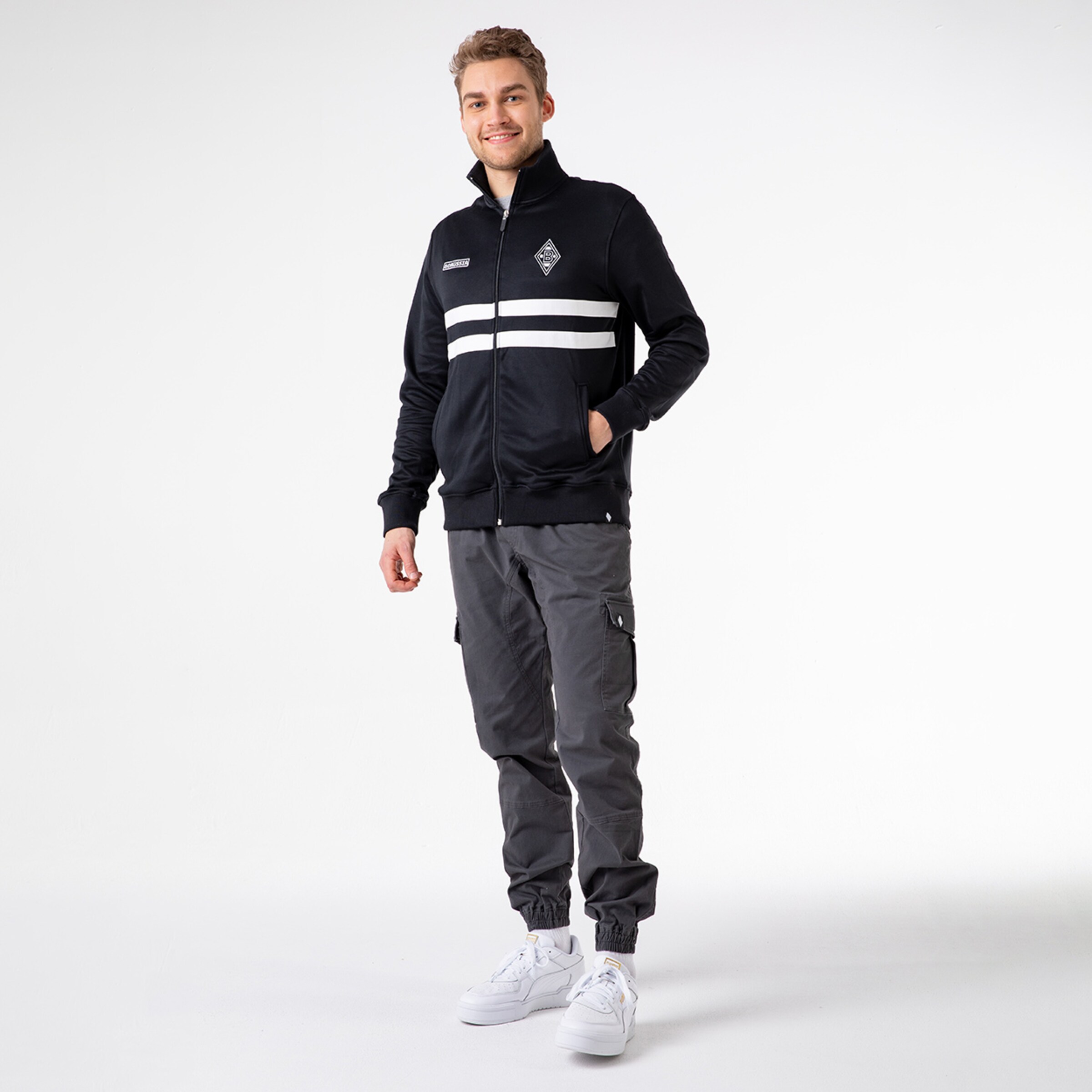 Junger Mann trägt eine schwarze Jacke mit weißen Streifen und graue Cargo-Hosen.