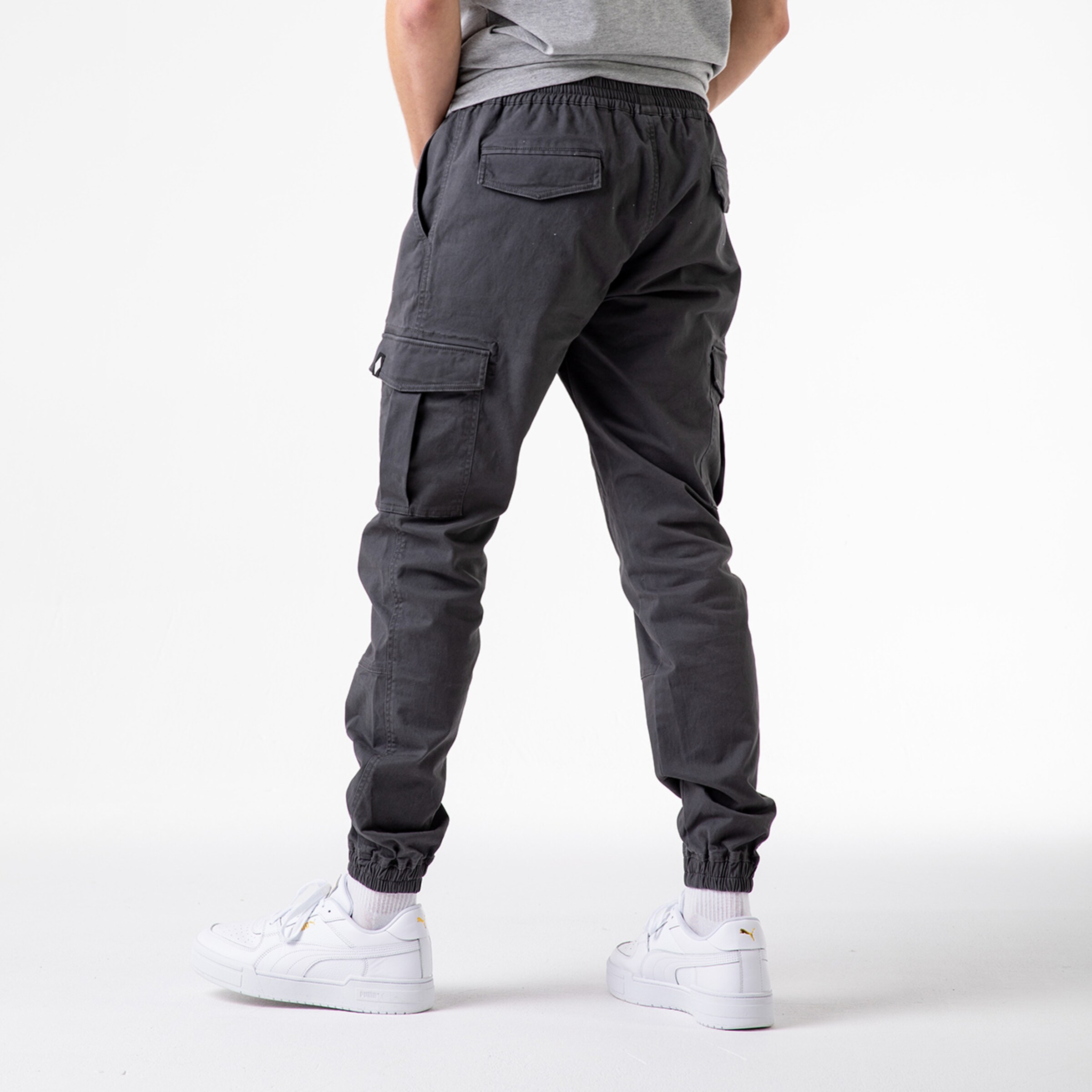 Person trägt graue Cargo-Hose mit elastischem Bund und weißen Sneakern von hinten.