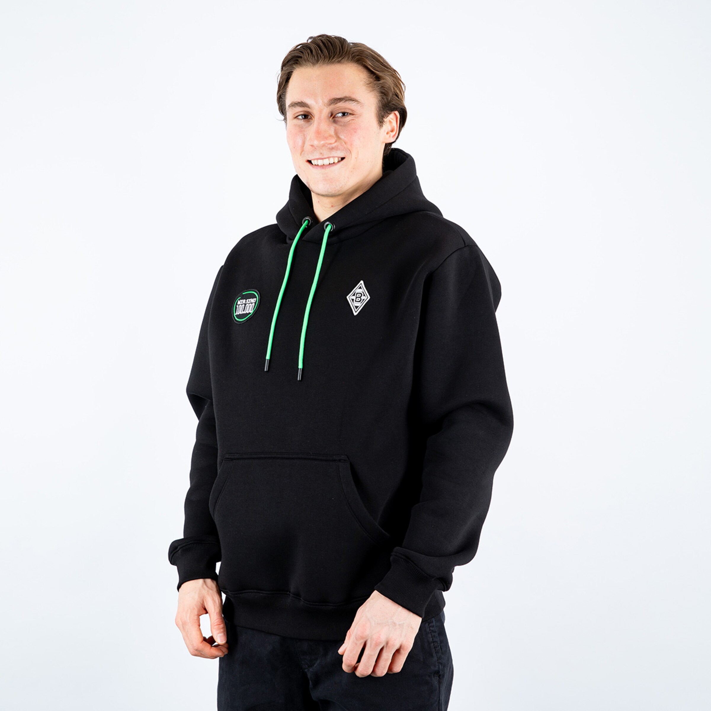 Ein junger Mann mit einem lächelnden Gesicht trägt einen schwarzen Hoodie mit grünen Details.