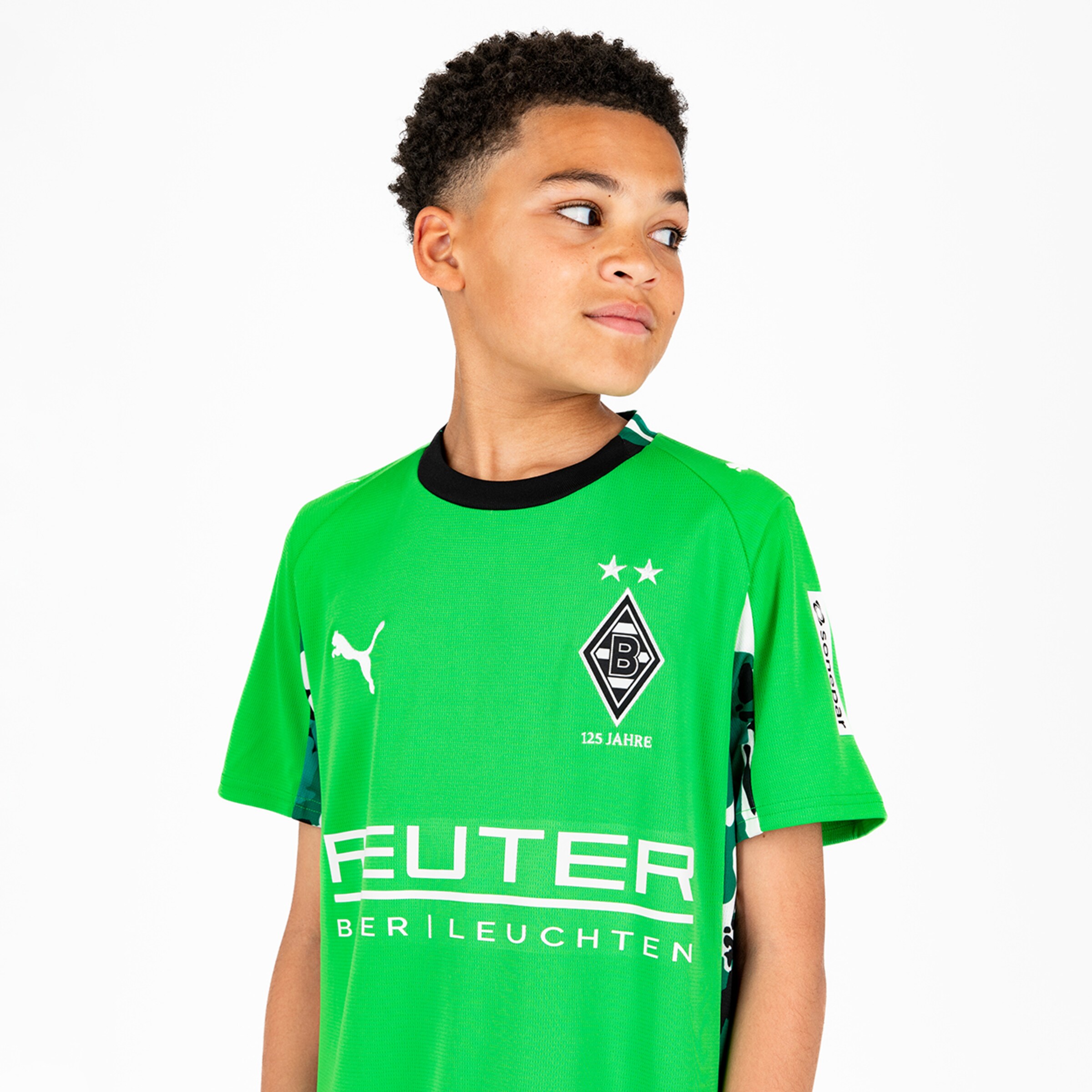 Ein Junge trägt ein grünes Borussia Mönchengladbach-Trikot mit einem lachenden Blick.