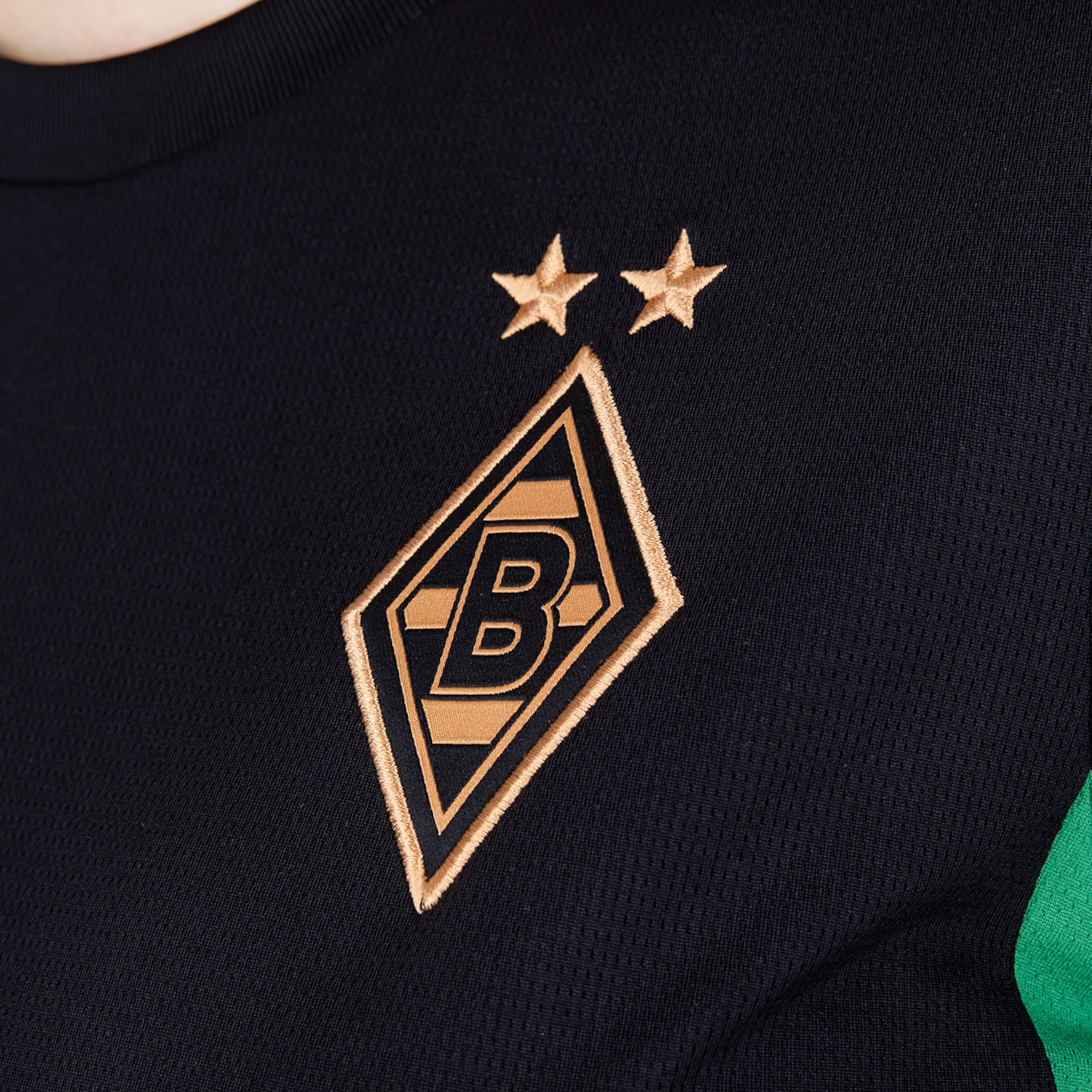 Gold besticktes Logo von Borussia Mönchengladbach auf schwarzem Stoff: Raute mit einem „B“ und zwei Sternen darüber.