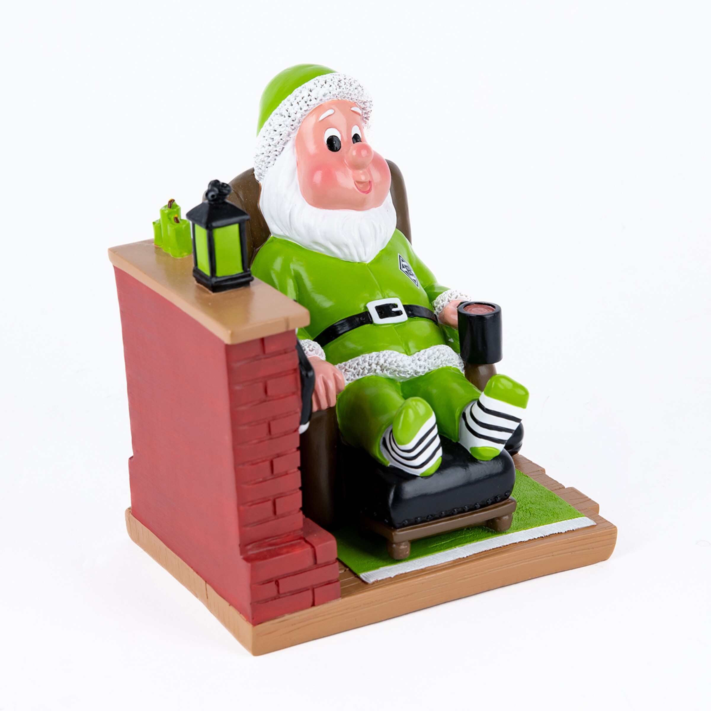 Weihnachtsmann-Figur in grünem Anzug sitzt im Sessel neben einem Kamin, trägt gestreifte Socken und hält eine Tasse.