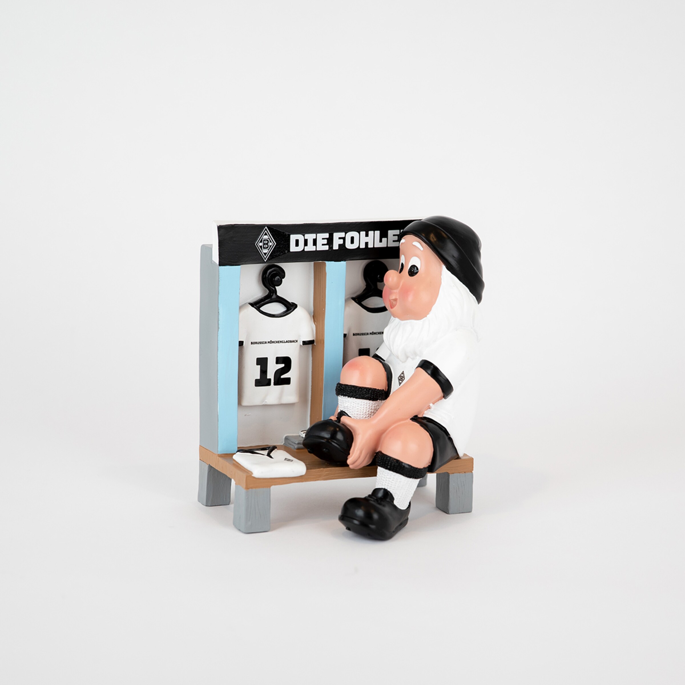 Eine Figur mit einem weißen Bart die in der Umkleide sitzt und Fußballschuhe anzieht neben einem Trikot mit der Nummer 12.