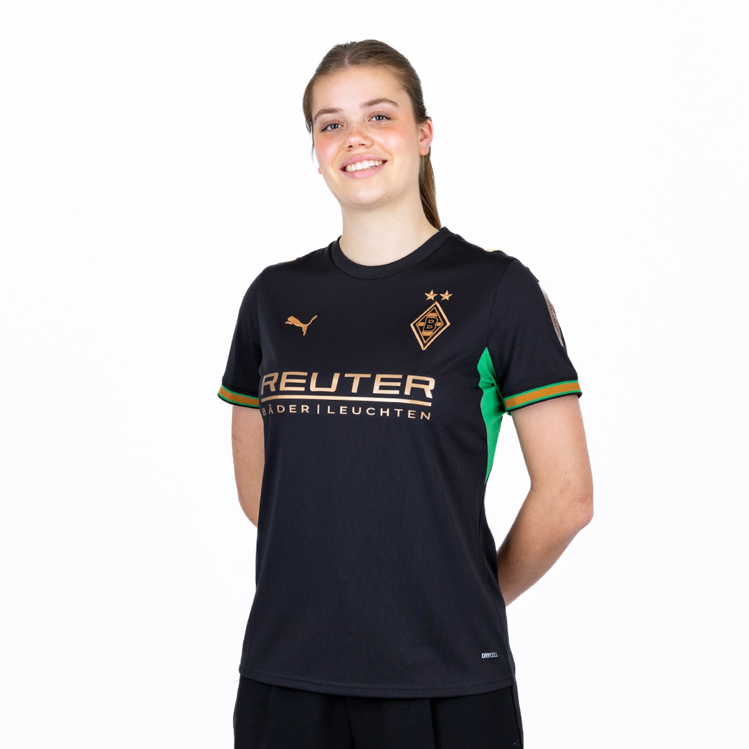 Lächelnde Fußballspielerin von Borussia Mönchengladbach im schwarzen Trikot mit goldenen Akzenten vor weißem Hintergrund.