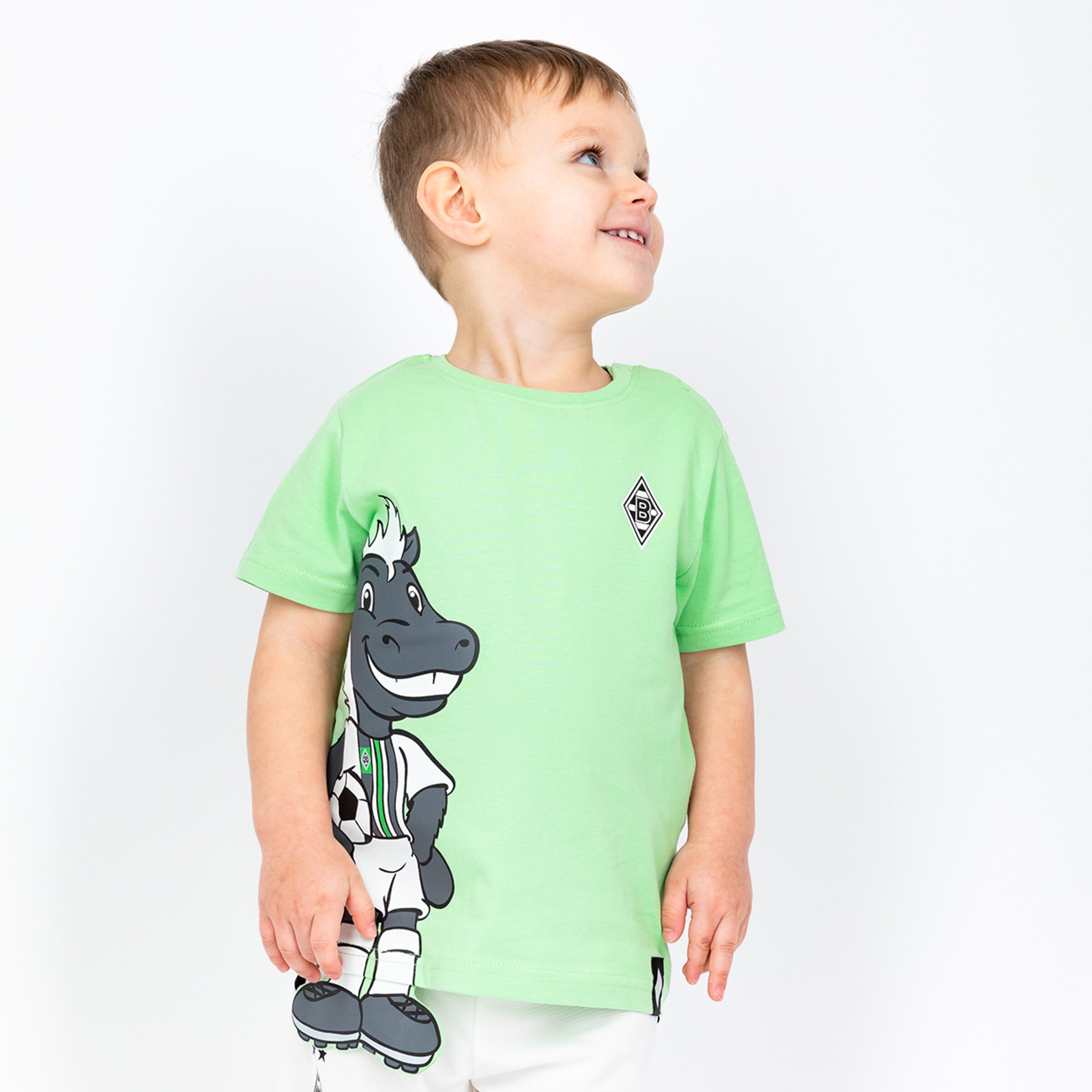 Ein lächelndes Kind trägt ein grünes T-Shirt mit dem Maskottchen von Borussia Mönchengladbach Jünter.