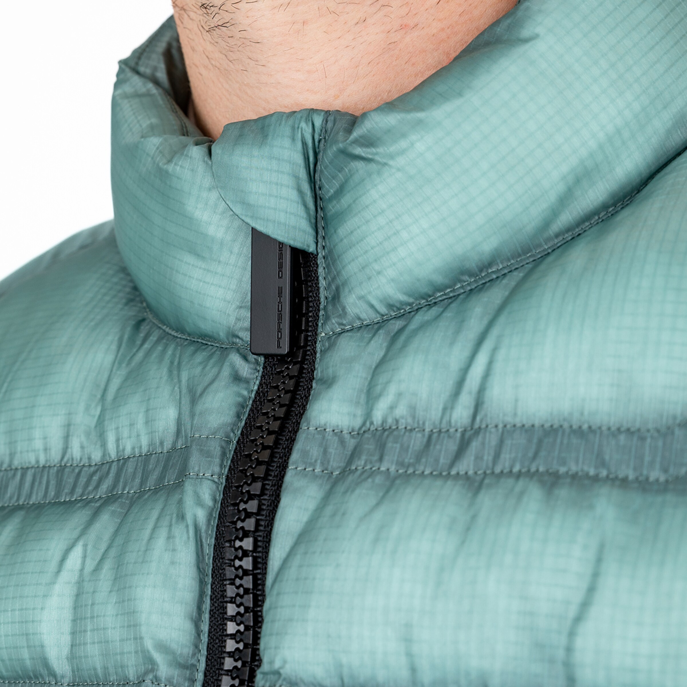 Nahaufnahme eines oberen Teils einer Jacke mit Reißverschluss grünlich und leicht glänzend.