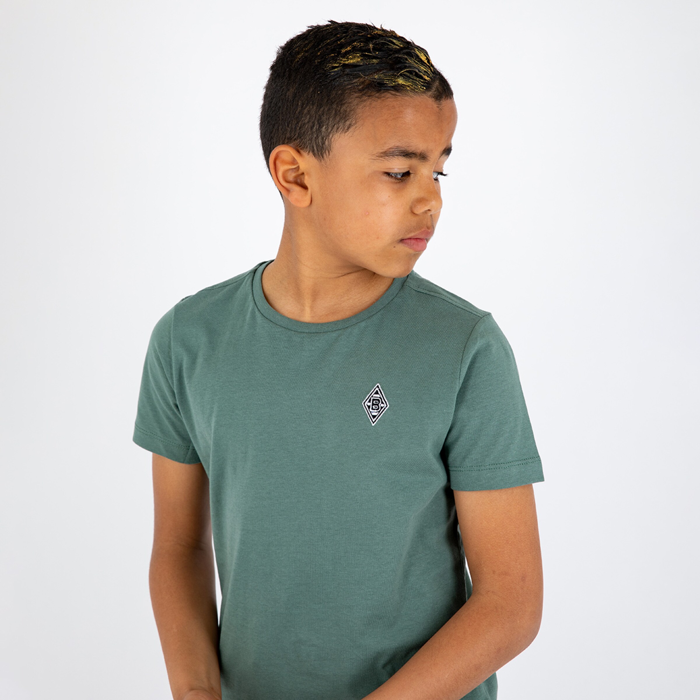 Junge mit kurzärmeligem grünem T-Shirt steht seitlich und blickt nach unten.