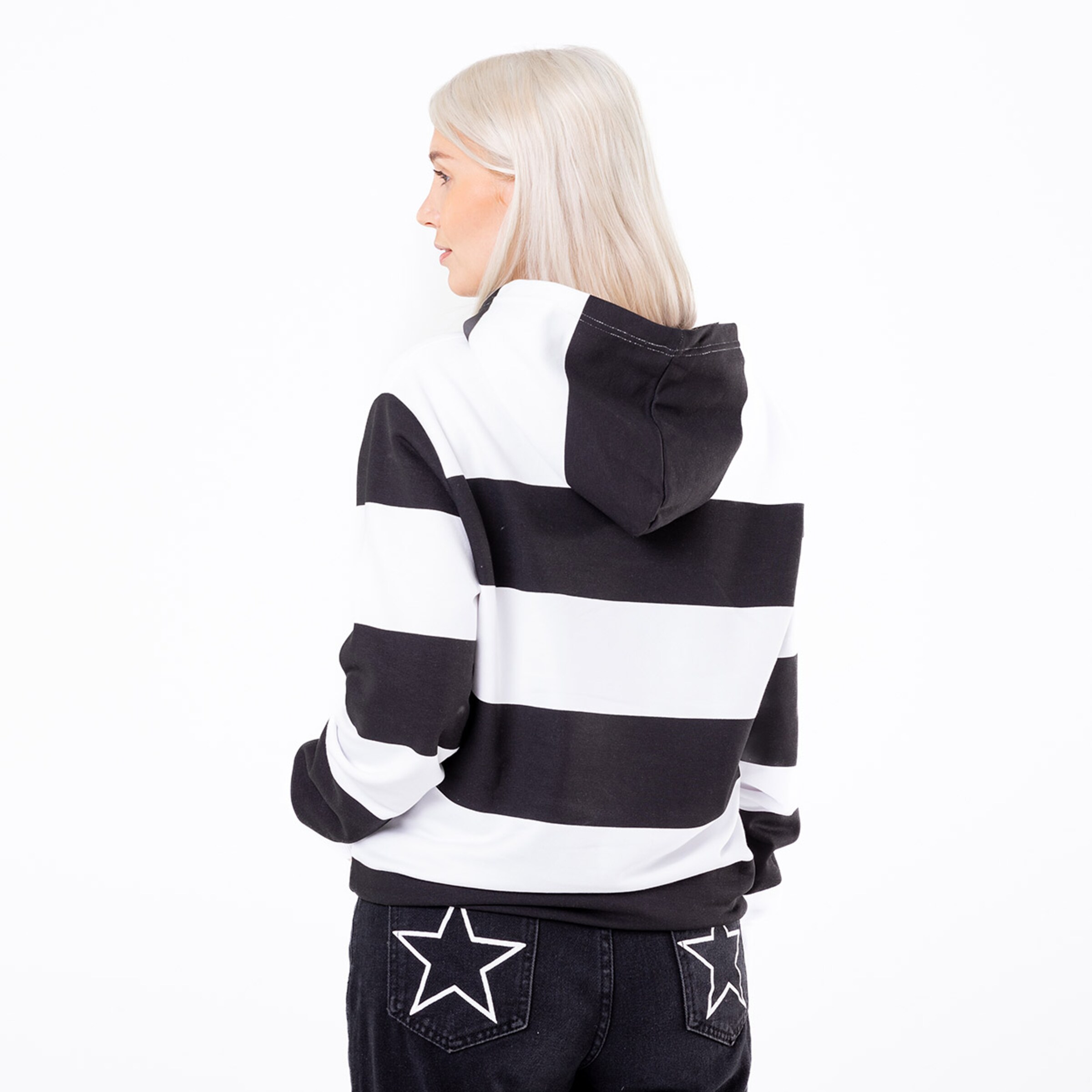 Eine Frau mit blonden Haaren trägt einen gestreiften Hoodie mit Kapuze blickt von hinten zur Kamera.