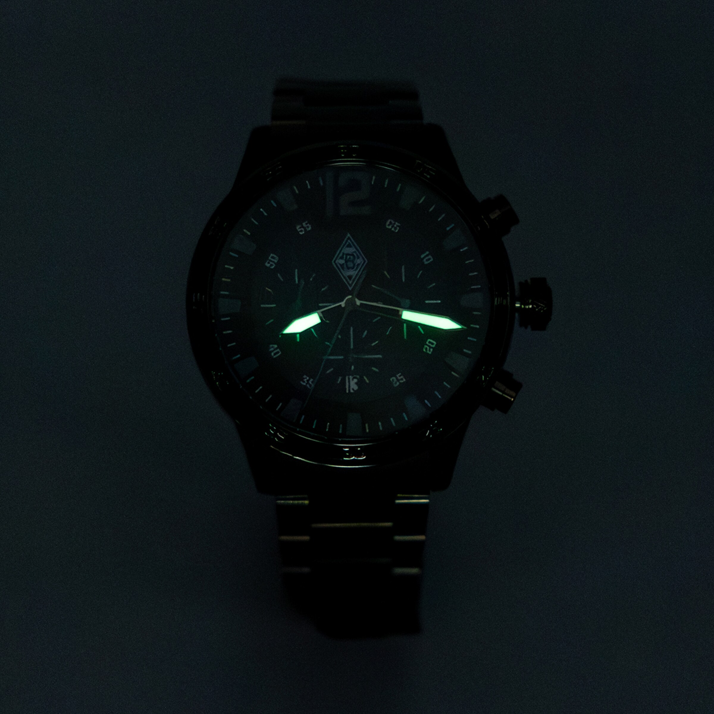 Schwarzer Chronograph im Dunkeln mit grün leuchtenden Zeigern und Borussia Mönchengladbach Logo auf dem Zifferblatt.