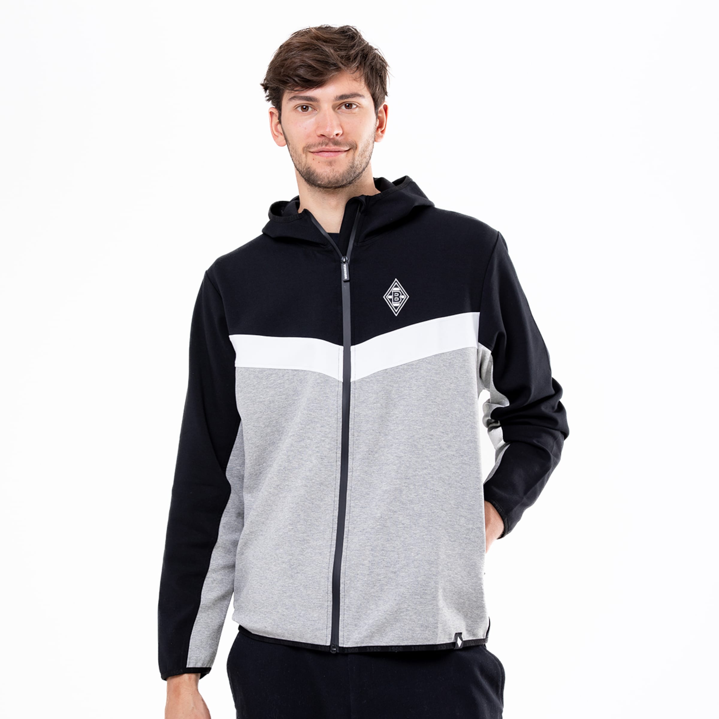 Ein Mann trägt eine graue und schwarze Jacke mit Kapuze und einem Borussia Mönchengladbach Logo.