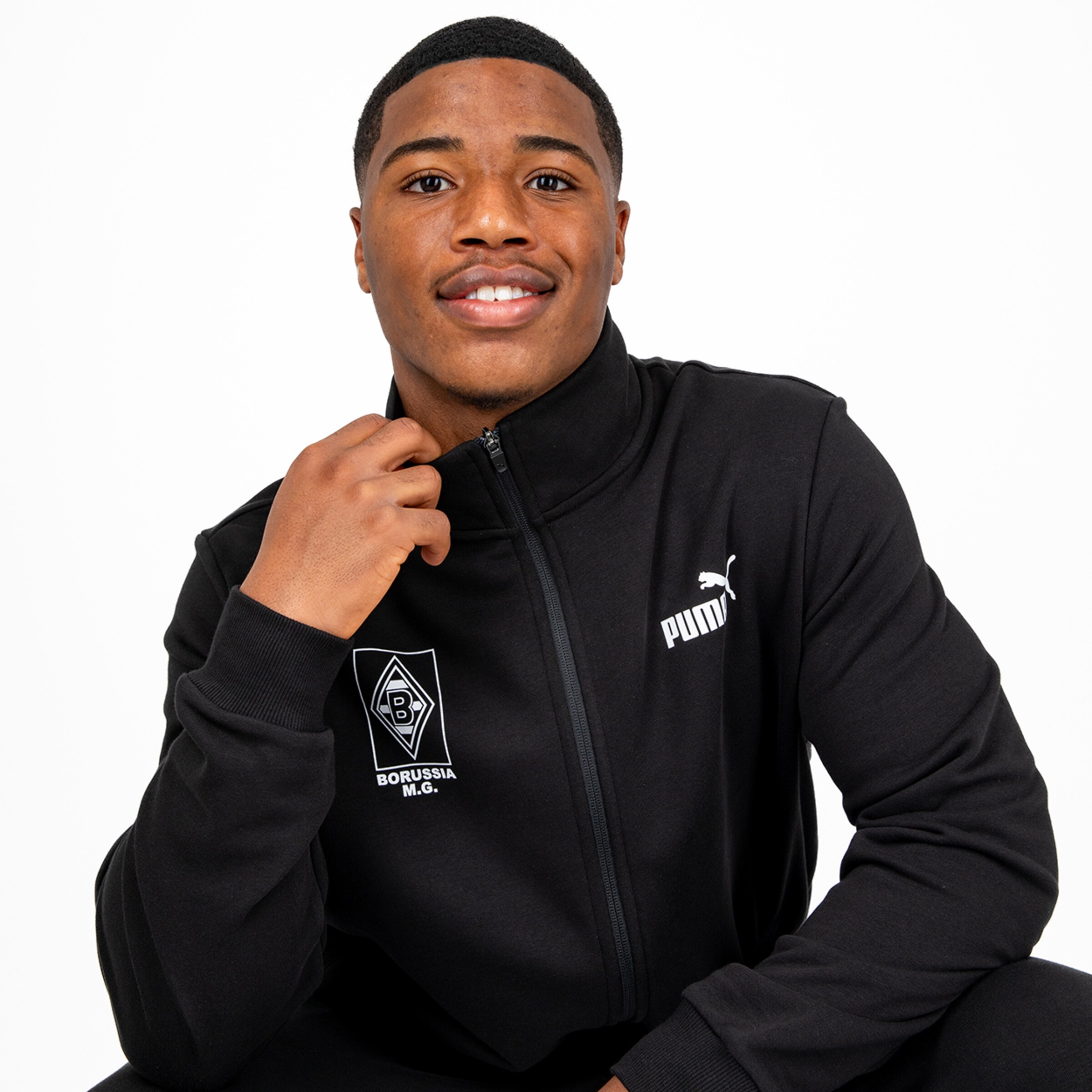 A young man in a black Puma jacket with the Borussia Mönchengladbach logo smiling at the camera.