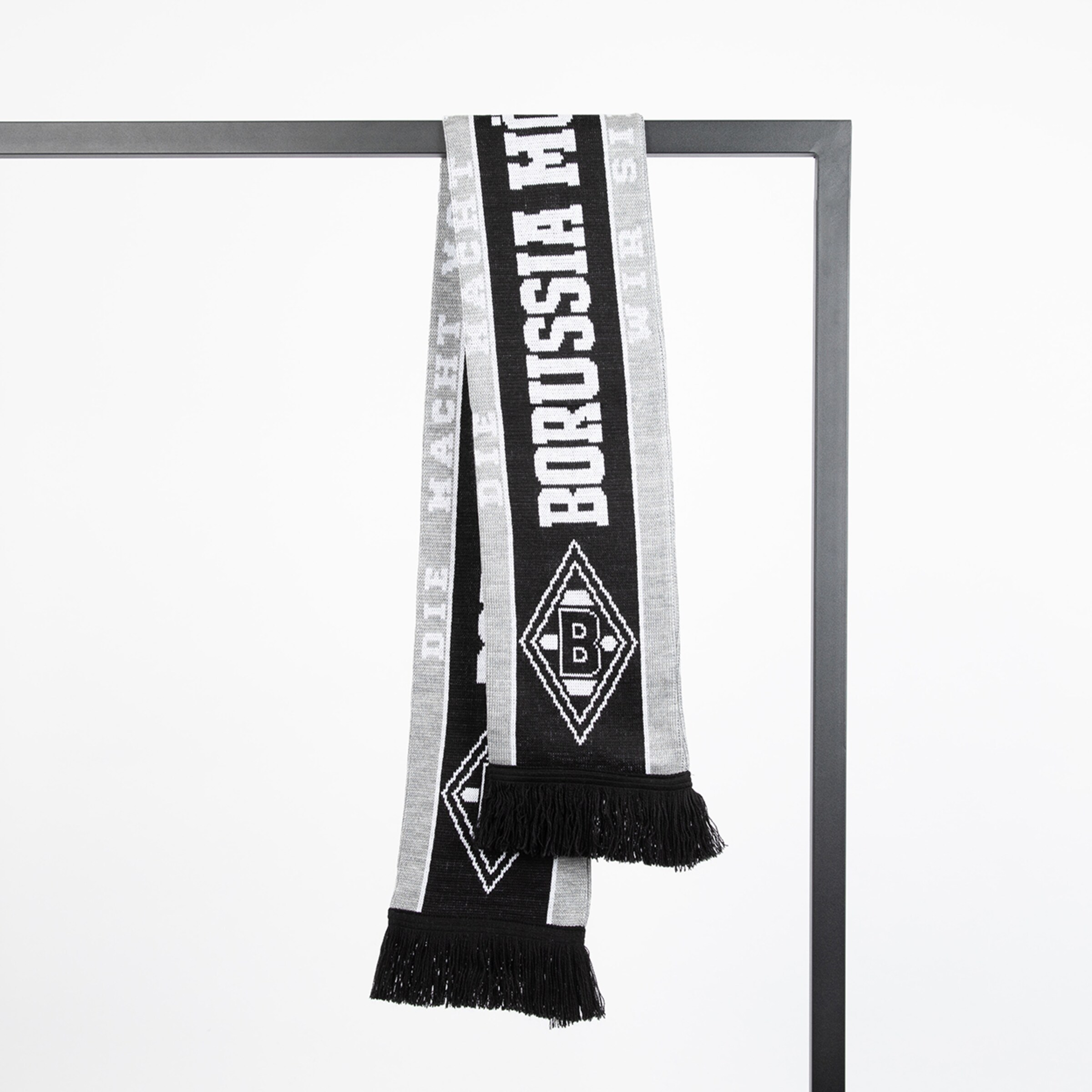 Schwarz-grauer Borussia Mönchengladbach Fanschal mit Vereinslogo und Schriftzug, hängend an einer Metallstange vor weißem Hintergrund.