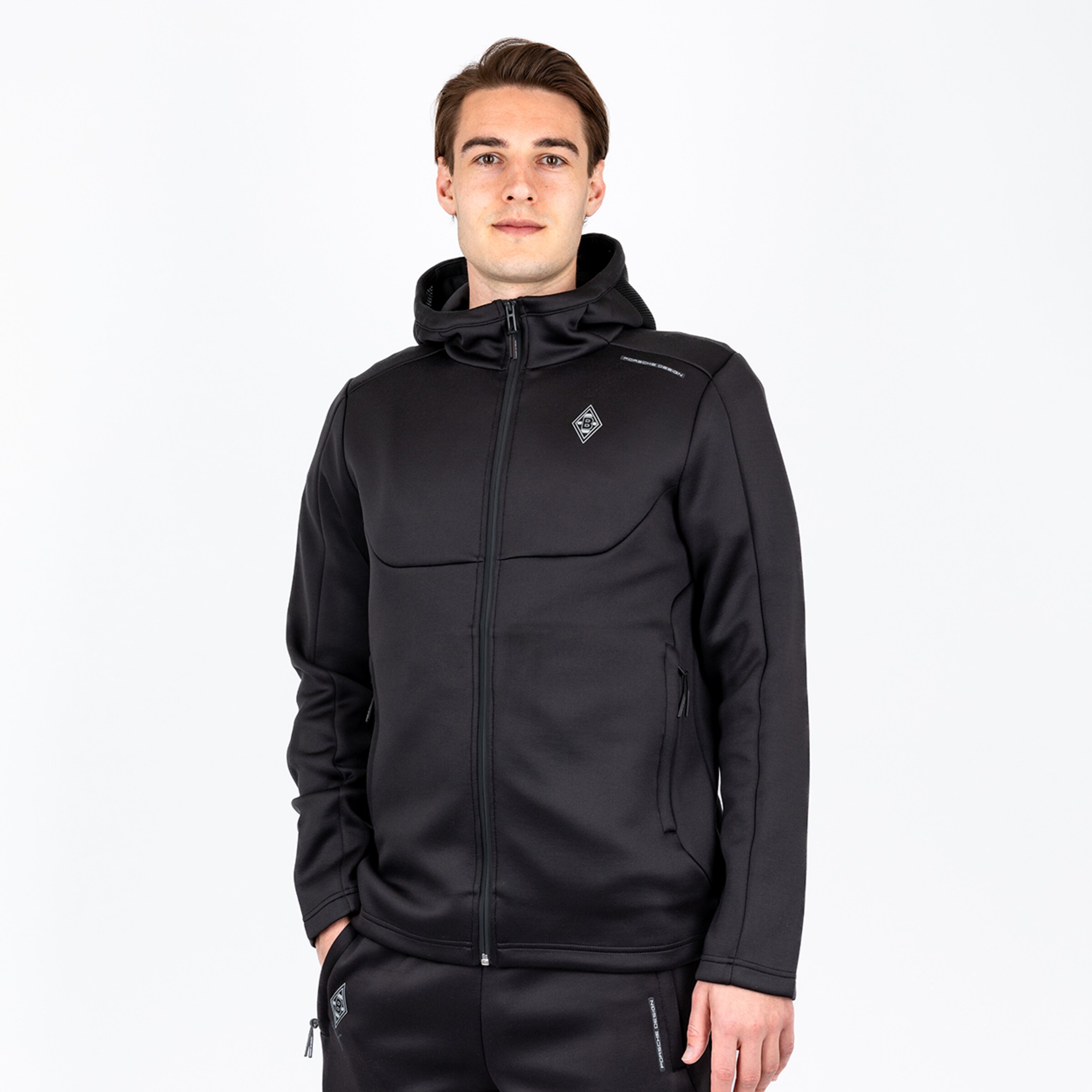 Mann trägt schwarze Sportjacke mit Kapuze und Zip; Logo von Borussia Mönchengladbach sichtbar.