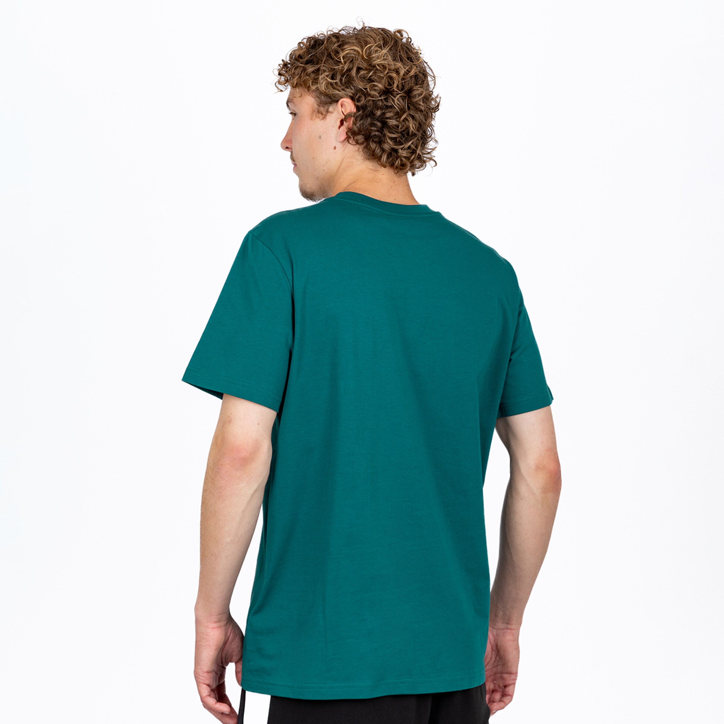 Ein junger Mann, von hinten und leicht nach links gedreht, trägt ein schlichtes, dunkelblaugrünes T-Shirt und schwarze Shorts. Er hat lockiges, hellbraunes Haar und blickt nach links. Der Hintergrund ist weiß.