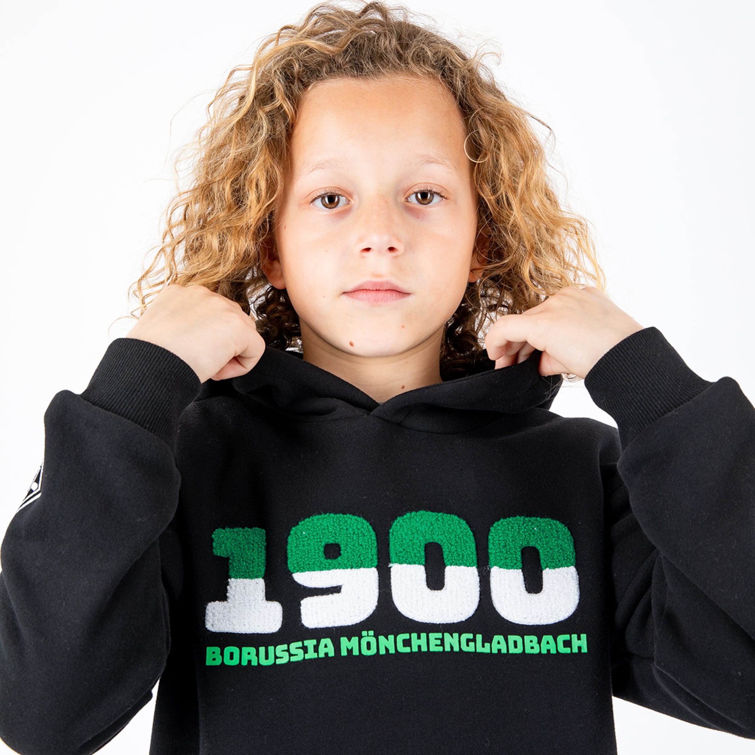 A boy with curly hair wears a black hoodie featuring 1900 Borussia Mönchengladbach.