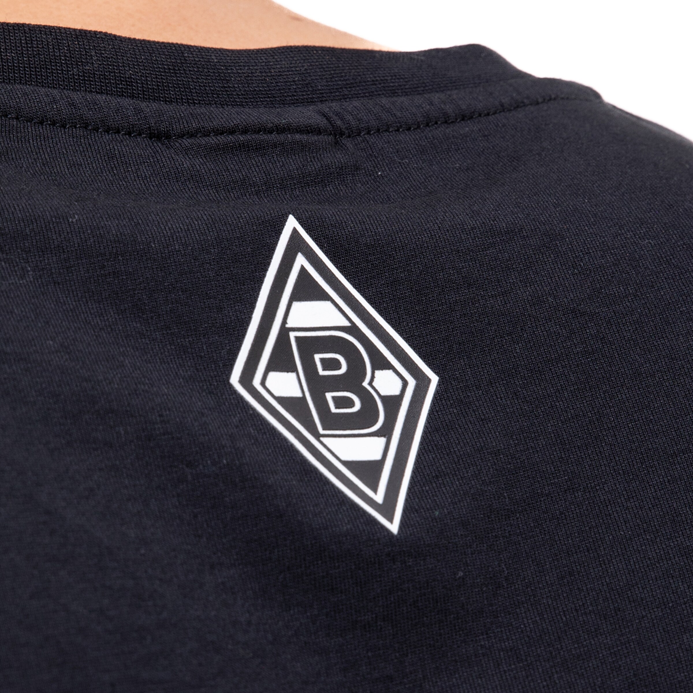 Nahaufnahme des Nackens eines schwarzen T-Shirts mit dem weißen Vereinslogo (Raute) von Borussia Mönchengladbach.