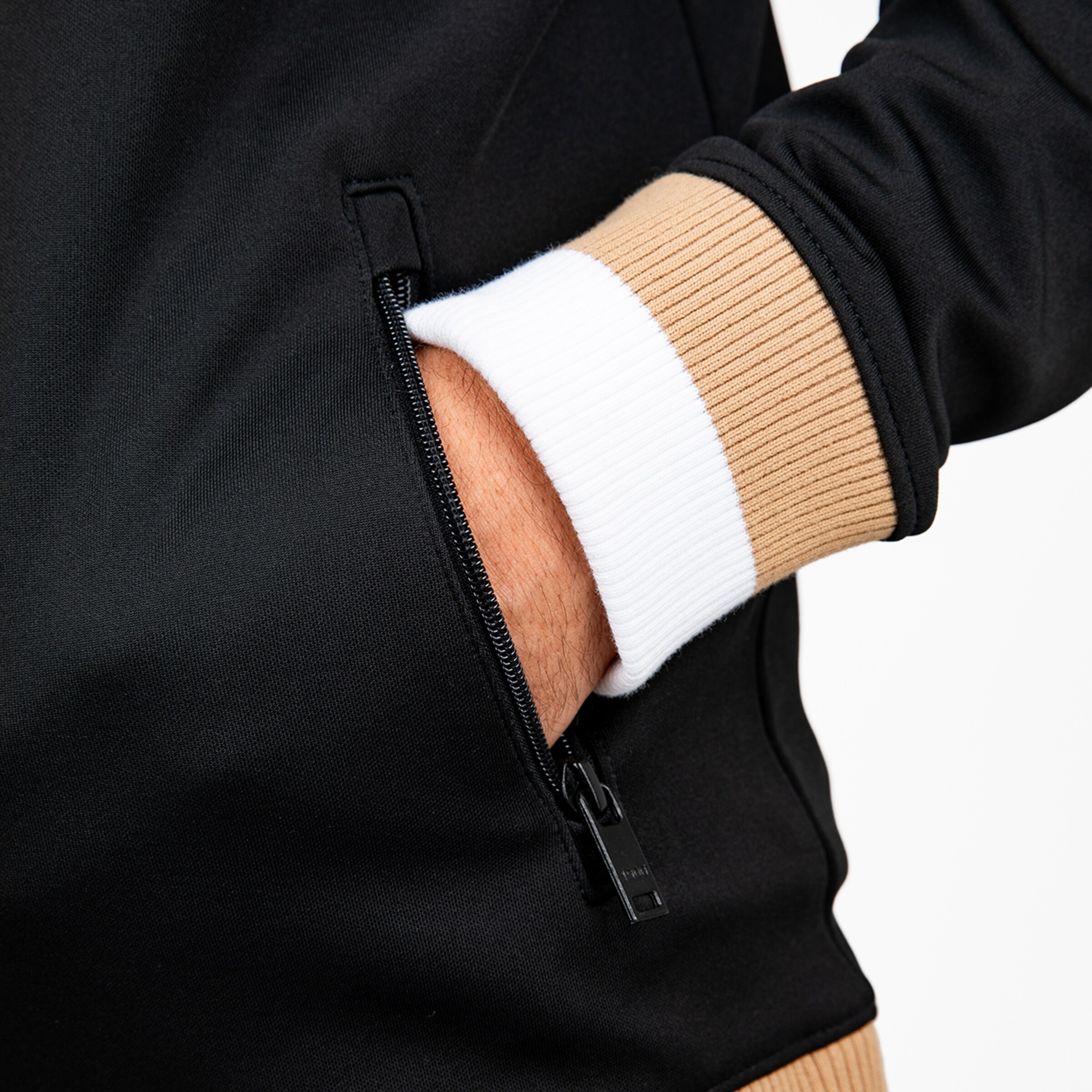 Nahaufnahme einer schwarzen Jacke mit Reißverschlusstasche und weiß-beigen Rippbündchen am Ärmel.