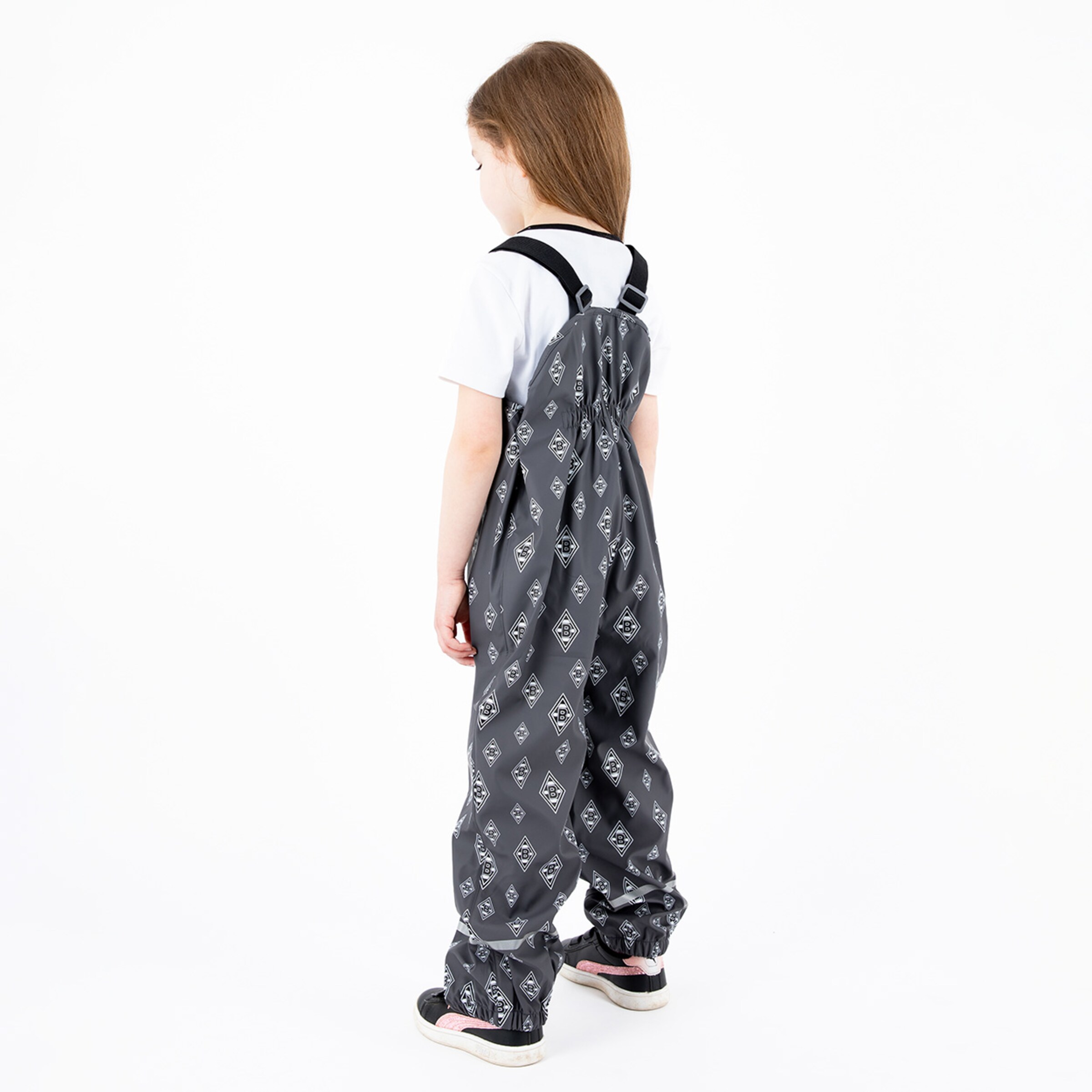 Ein Kind trägt einen grauen Overall mit Muster steht mit dem Rücken zur Kamera.