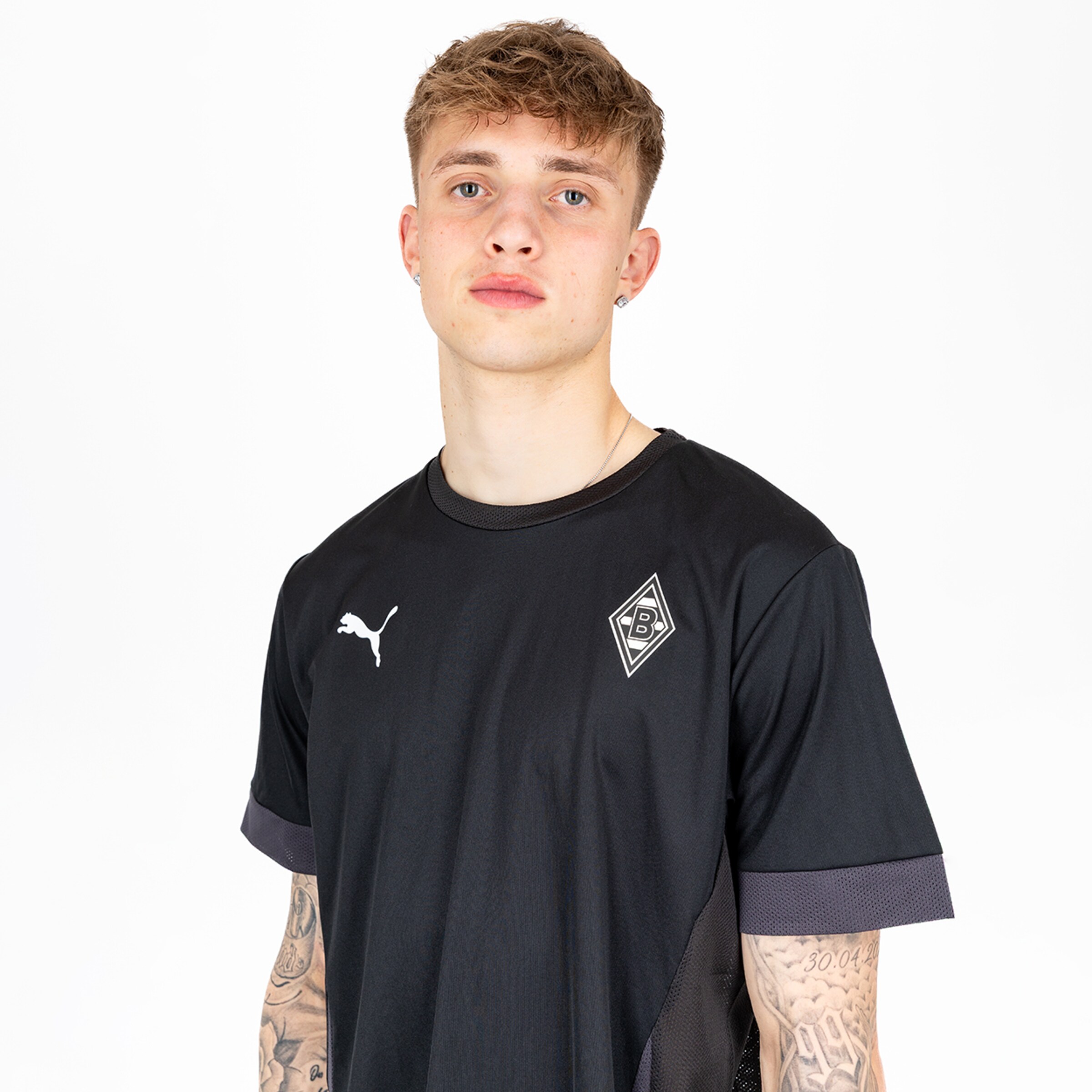 Young man with tattooed arms wearing a black Borussia Mönchengladbach T-shirt with Puma logo.