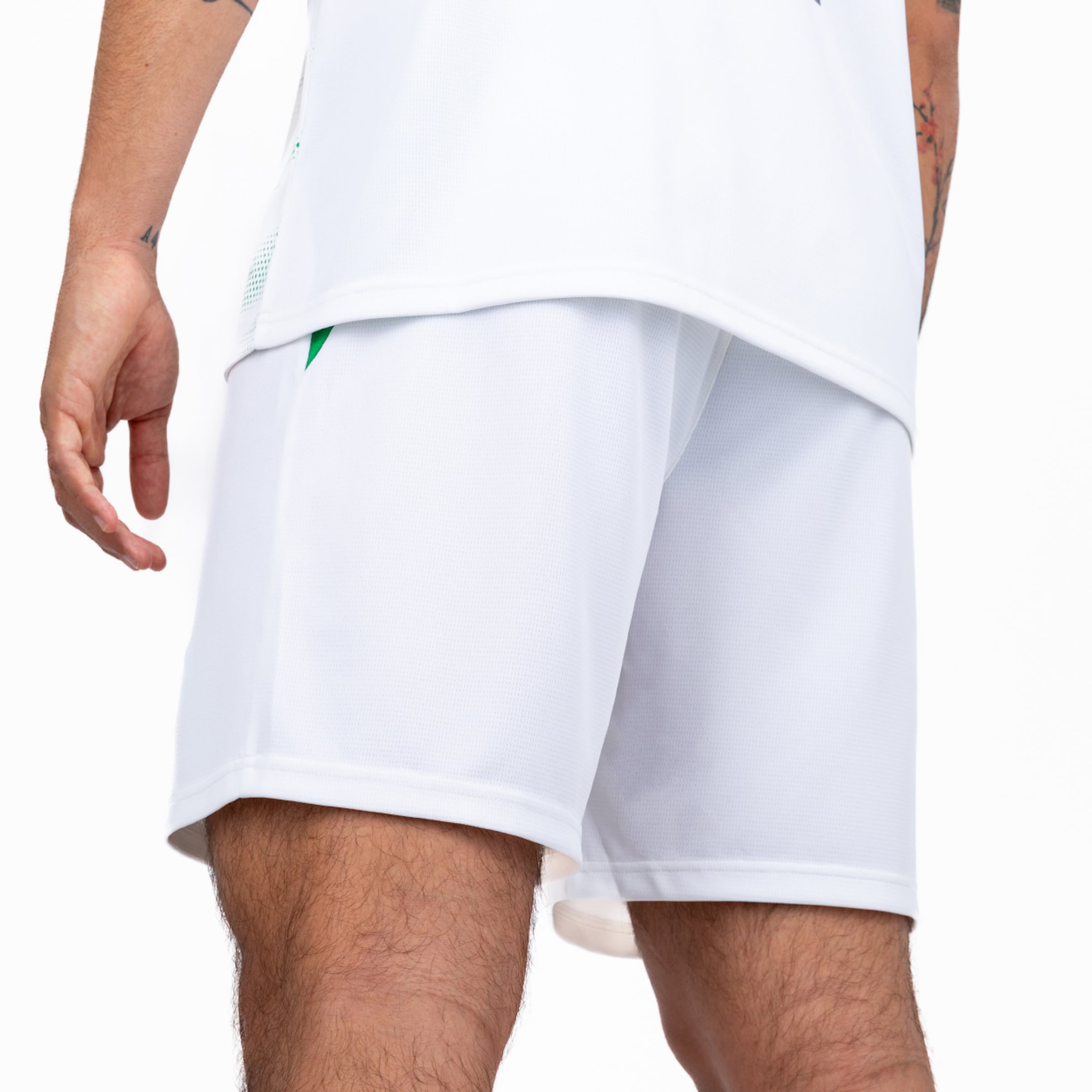 Nahaufnahme einer Person in weißen Sportshorts und passendem Trikot mit grünen Akzenten vor weißem Hintergrund.