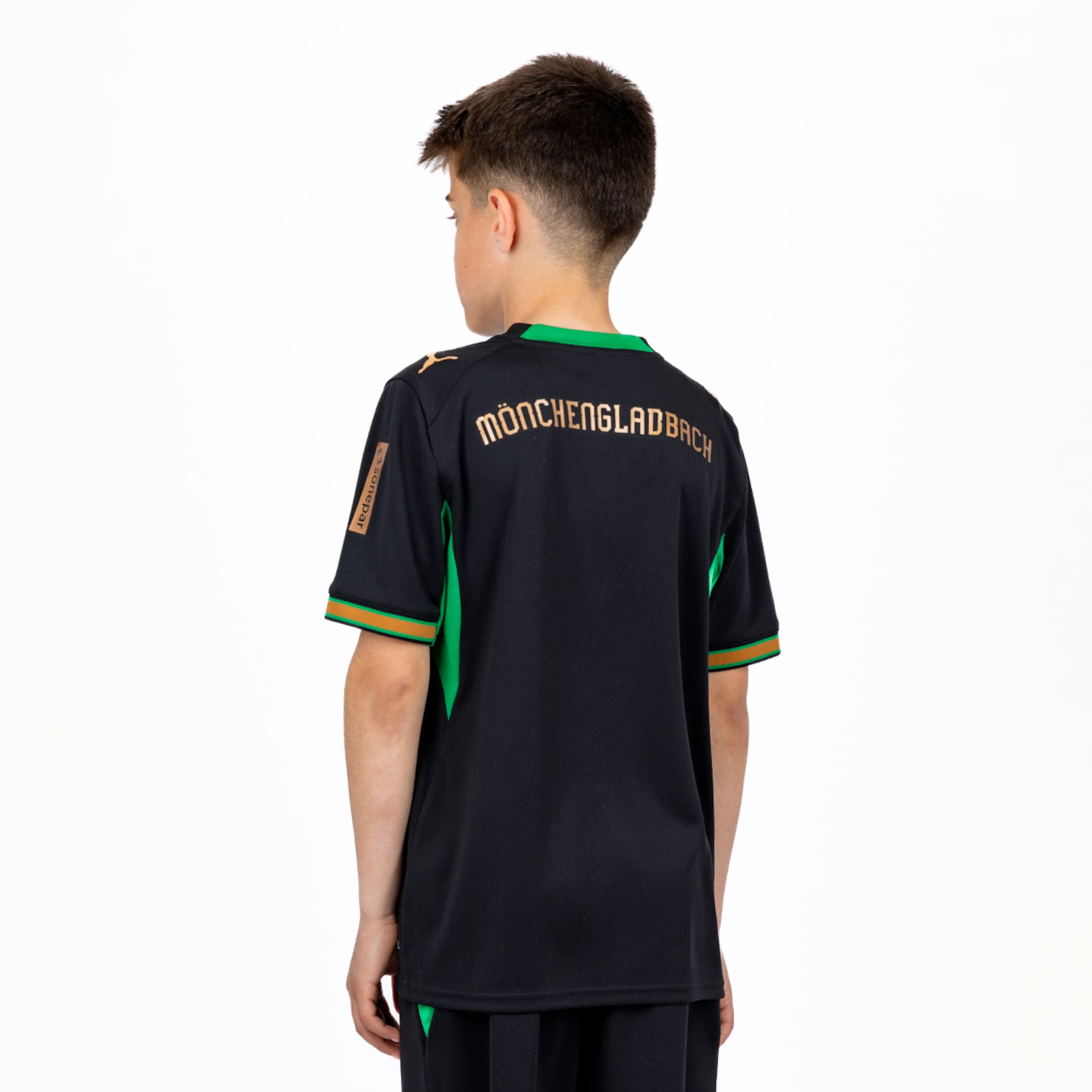 Rückansicht eines Jungen in einem schwarzen Mönchengladbach-Trikot mit goldenem Schriftzug und grünen Akzenten vor weißem Hintergrund.