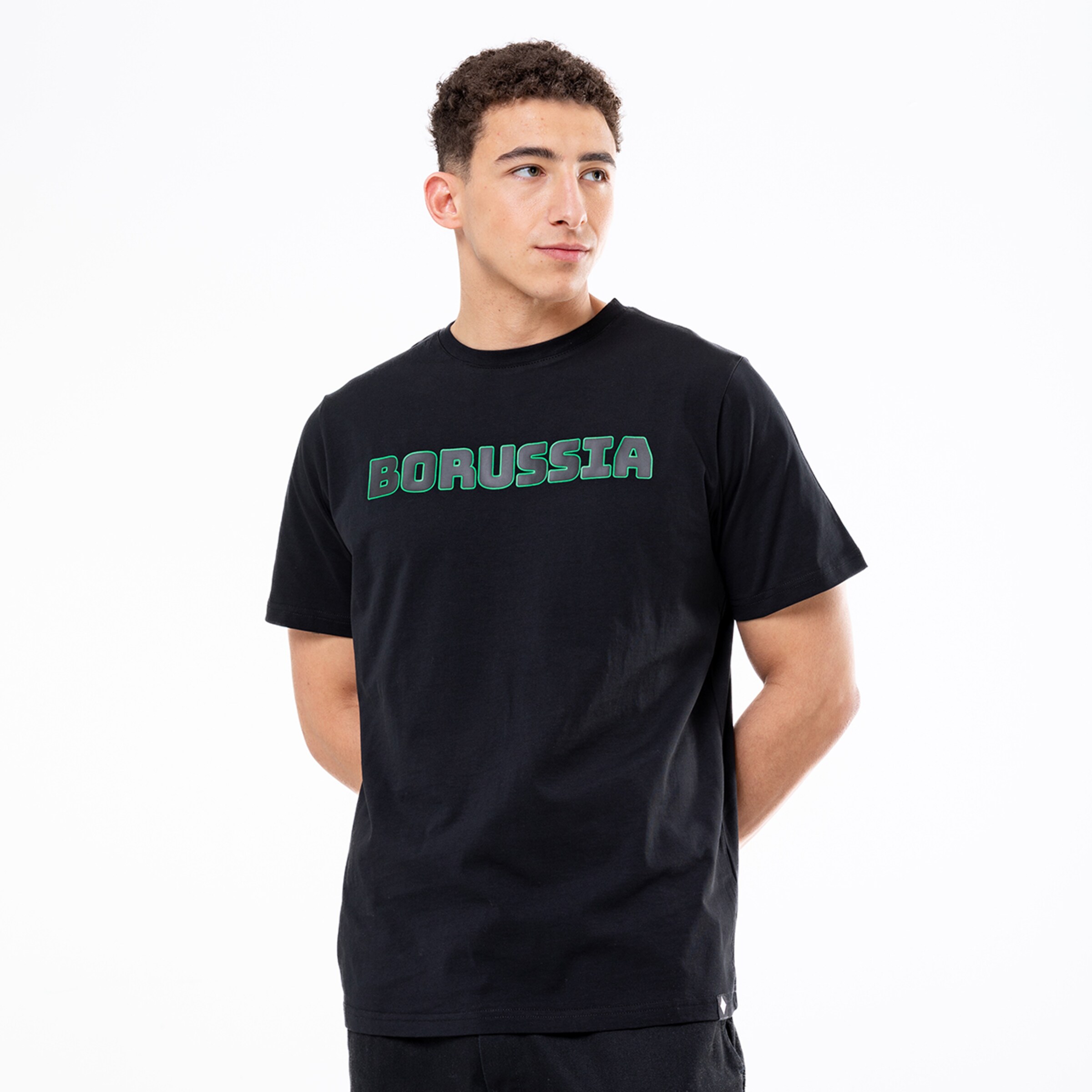 Junger Mann in einem schwarzen T-Shirt mit grünem „BORUSSIA“-Schriftzug vor weißem Hintergrund.
