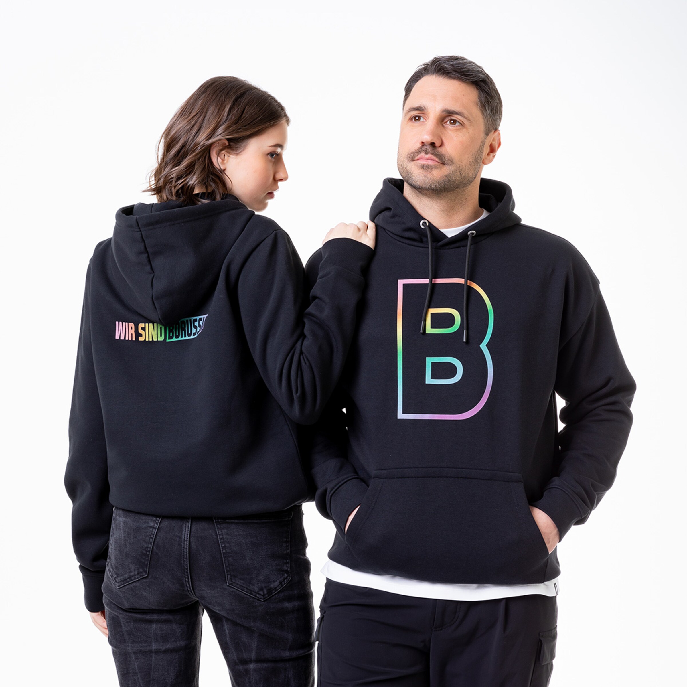 Zwei Personen in passenden schwarzen Hoodies mit buntem Logo.