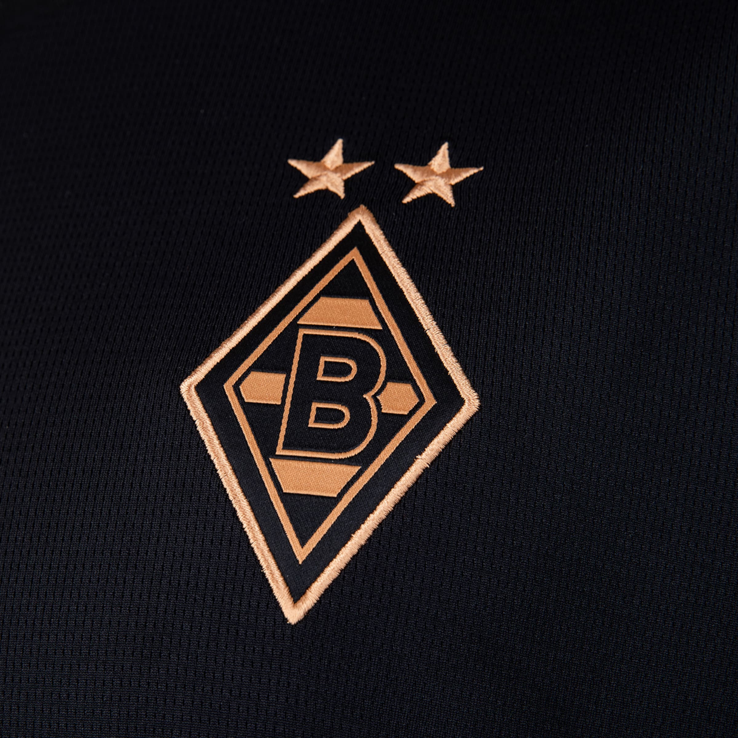 Goldfarben gesticktes Logo von Borussia Mönchengladbach mit zwei Sternen über der Raute auf schwarzem Textil.