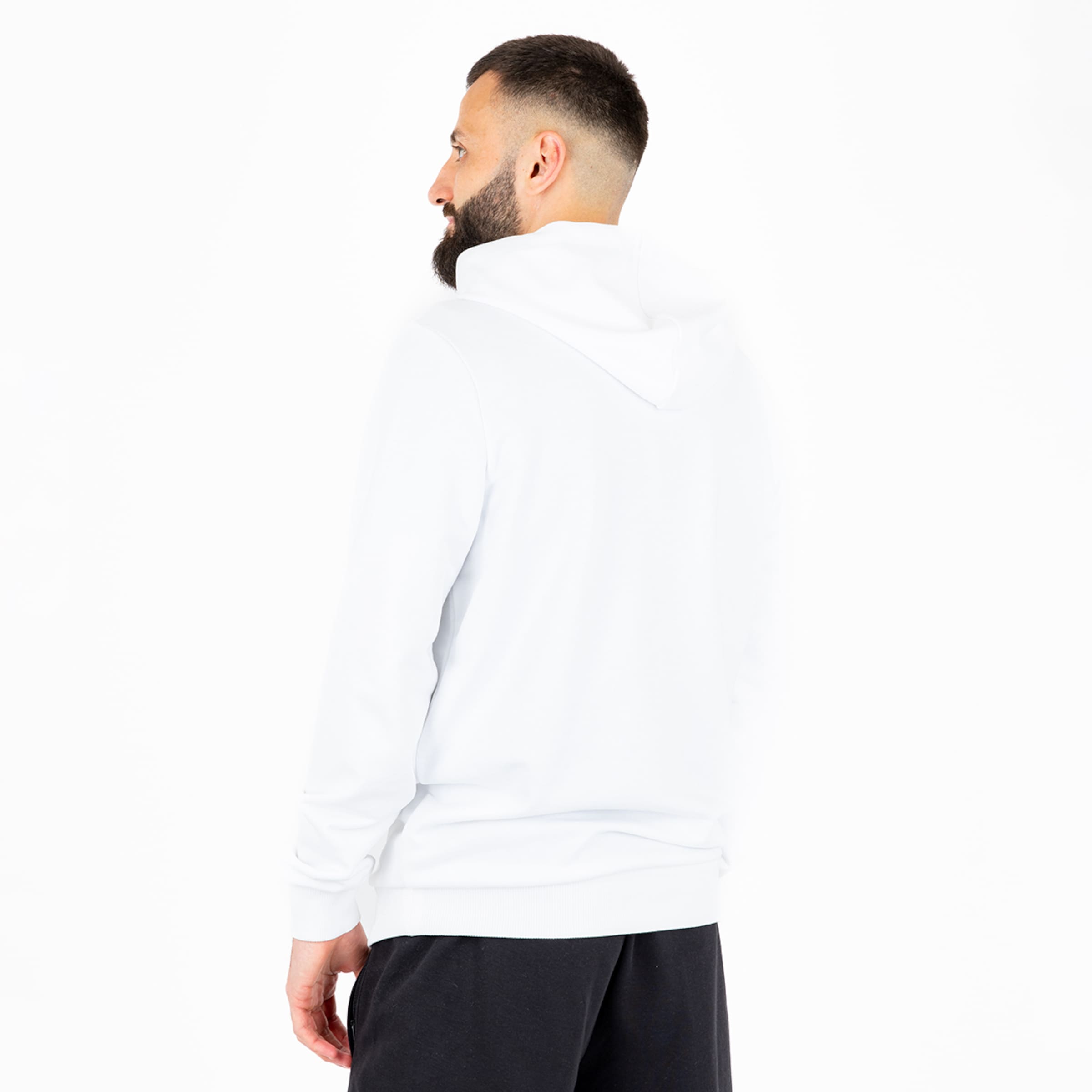 Back view of a bearded man wearing a white hoodie and black pants against a white background.