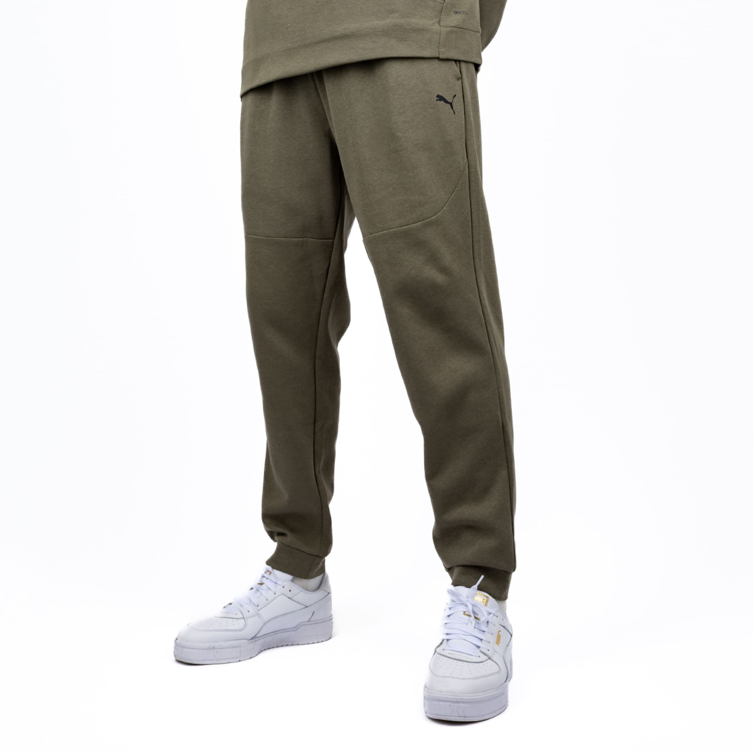 Olivgrüne Puma-Jogginghose mit Ziernähten und Logo sowie weiße Puma-Sneaker auf weißem Hintergrund.