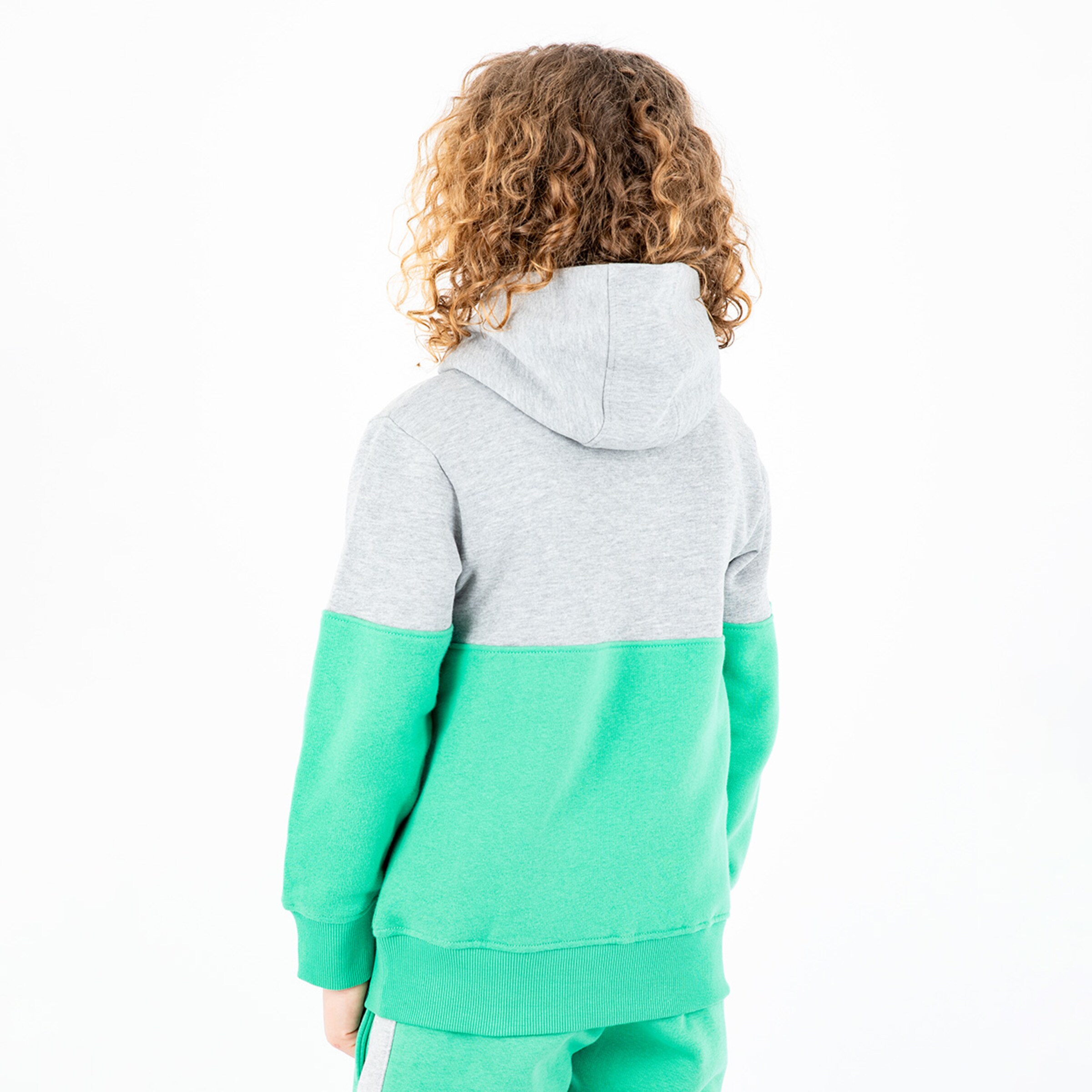 Junge mit lockigen Haaren trägt einen grauen und grünen Hoodie von hinten.