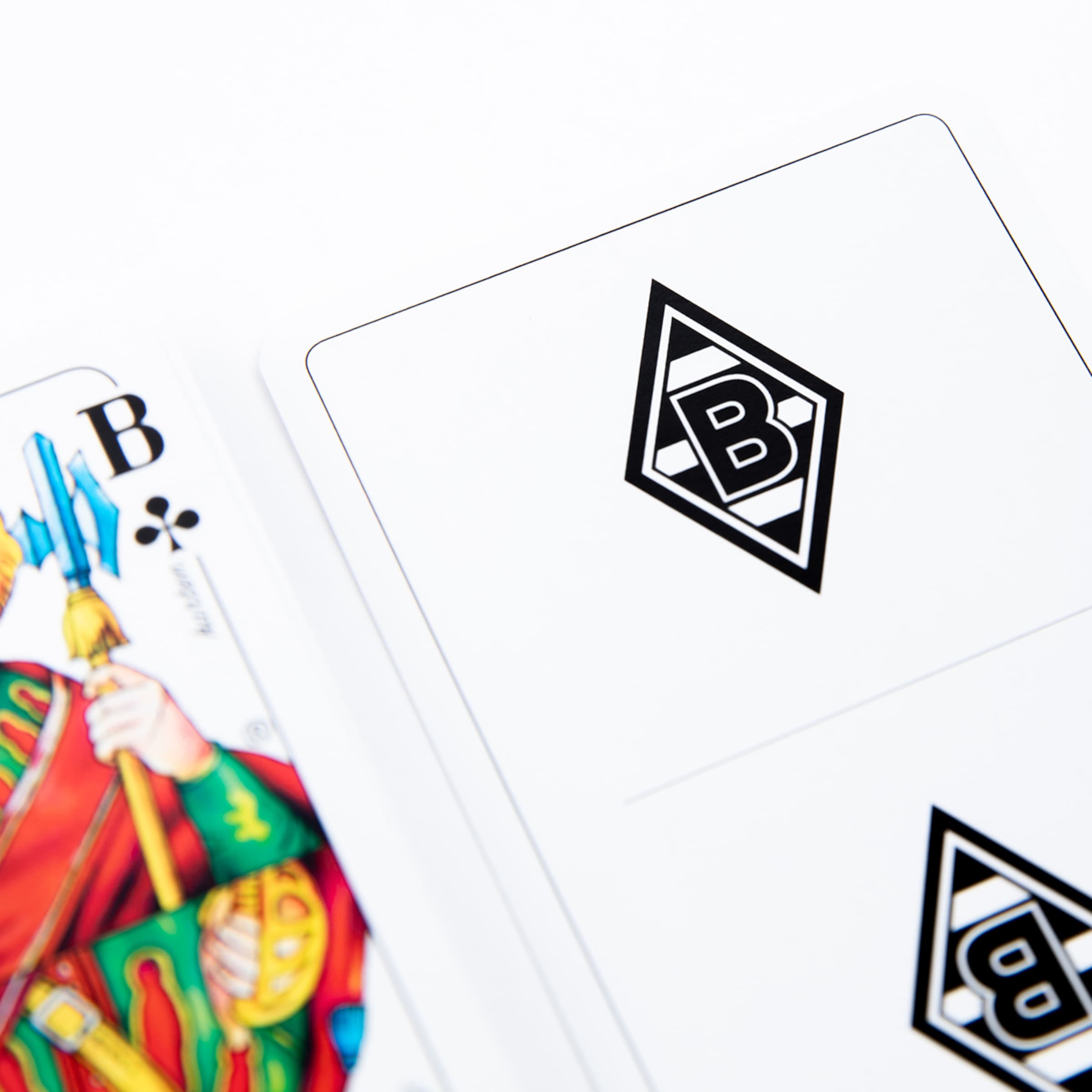 Nahaufnahme einer Kreuz-Bube-Spielkarte neben einer Karte mit dem Logo von Borussia Mönchengladbach auf weißem Hintergrund.