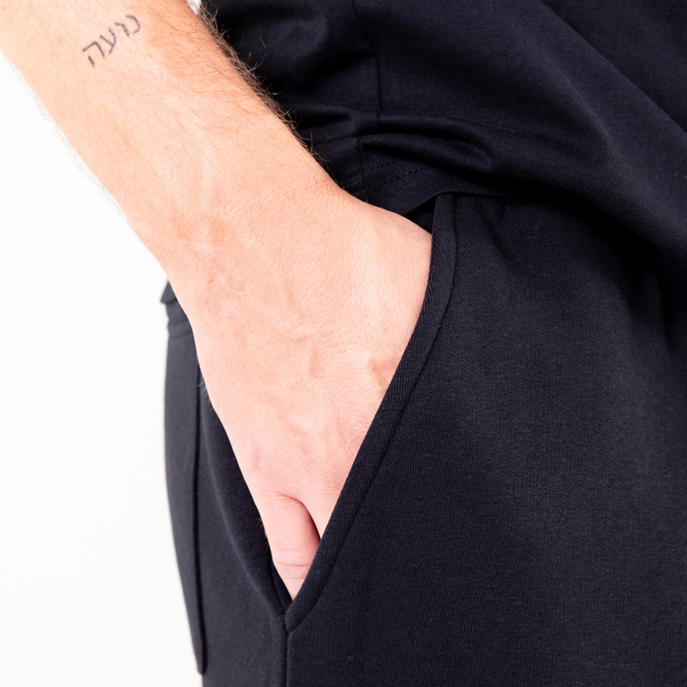 Nahaufnahme eines Fingers der in die Tasche eines schwarzen Kleidungsstücks eingreift mit einem sichtbaren Tattoo