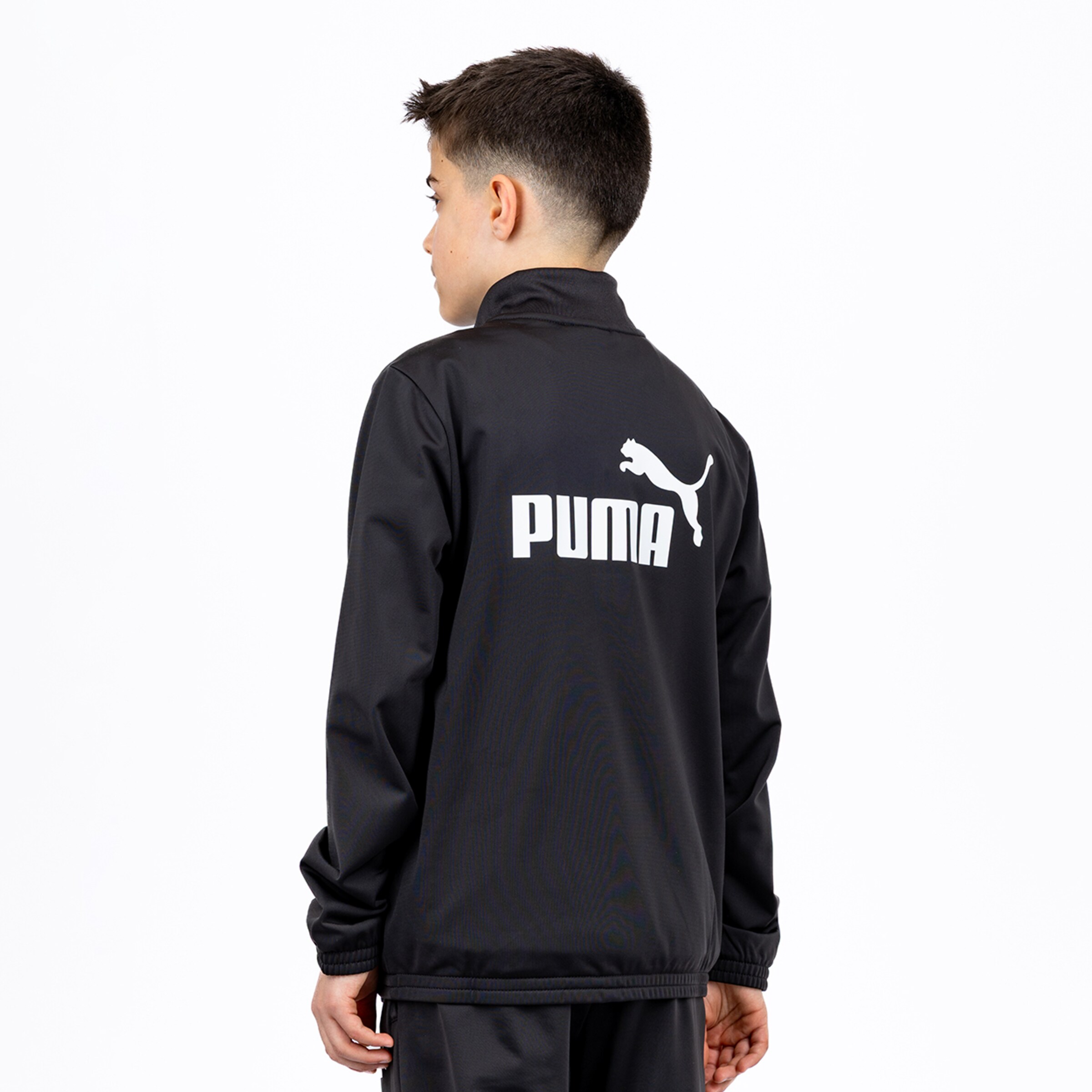 A boy from behind wearing a black Puma tracksuit jacket with a large white logo and wordmark on the back.