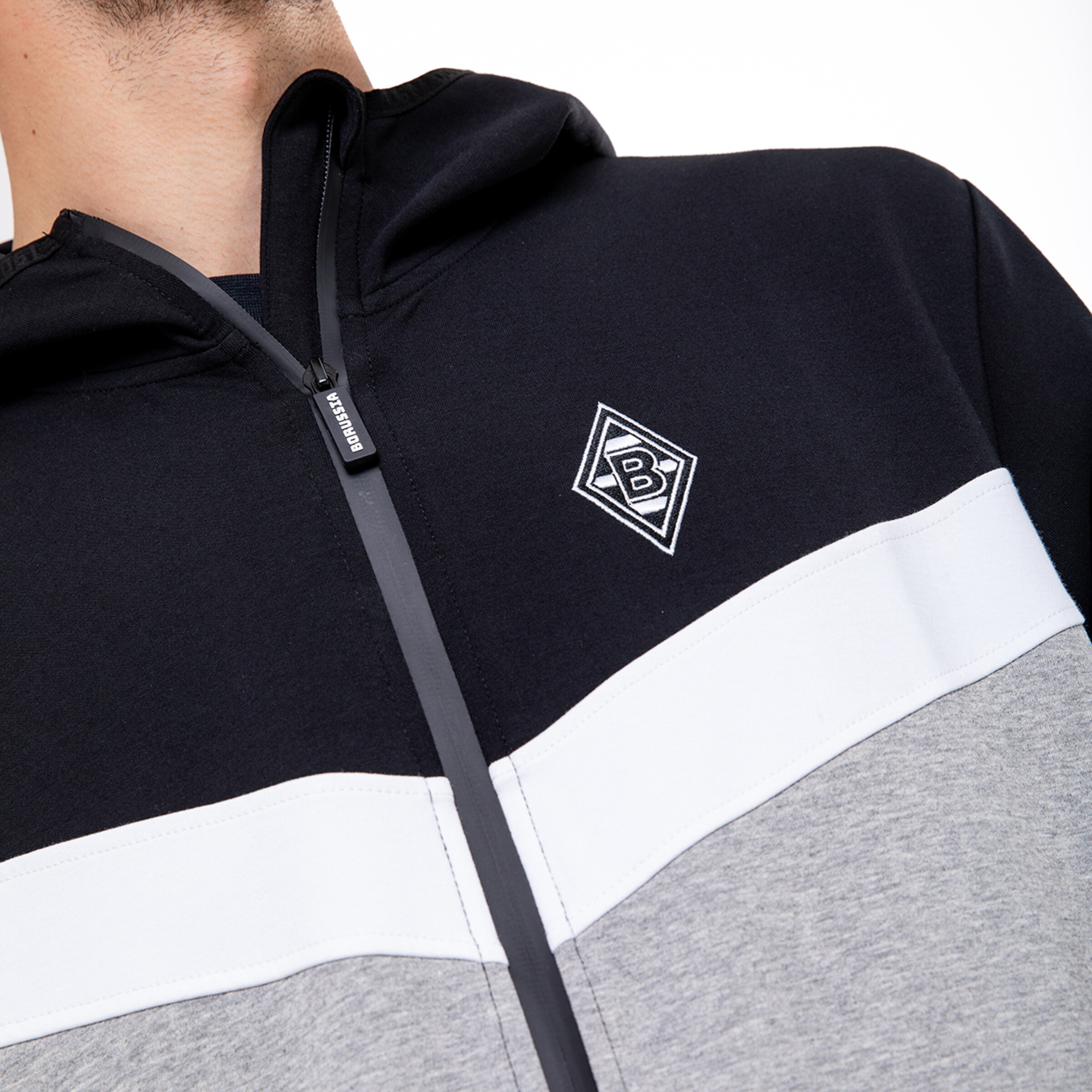 Ein sportliches Oberteil mit einem Reißverschluss und Kapuze in schwarz weiß und grau mit dem Borussia Mönchengladbach Logo.