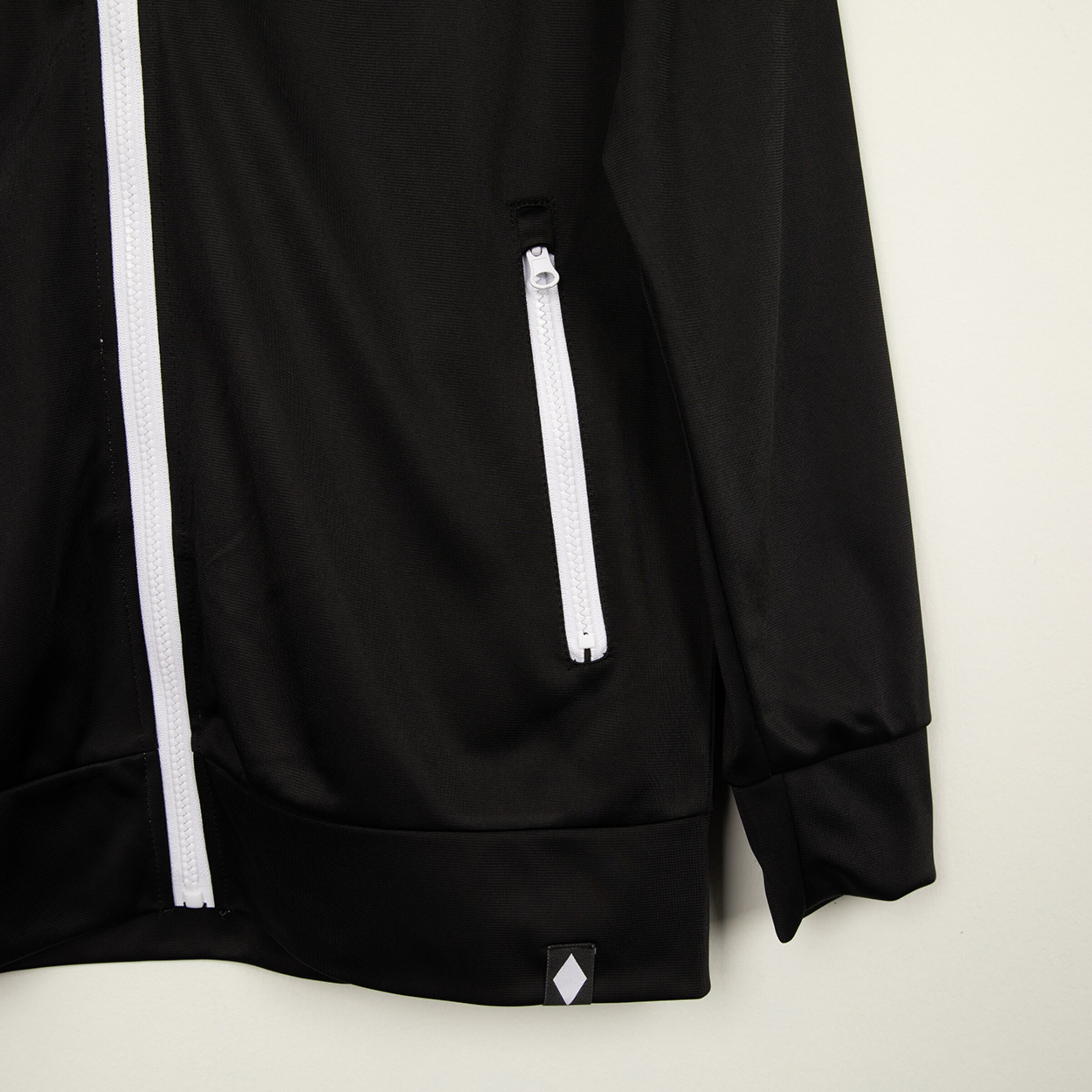 Schwarze Jacke mit weißen Reißverschlüssen und seitlichen Taschen.