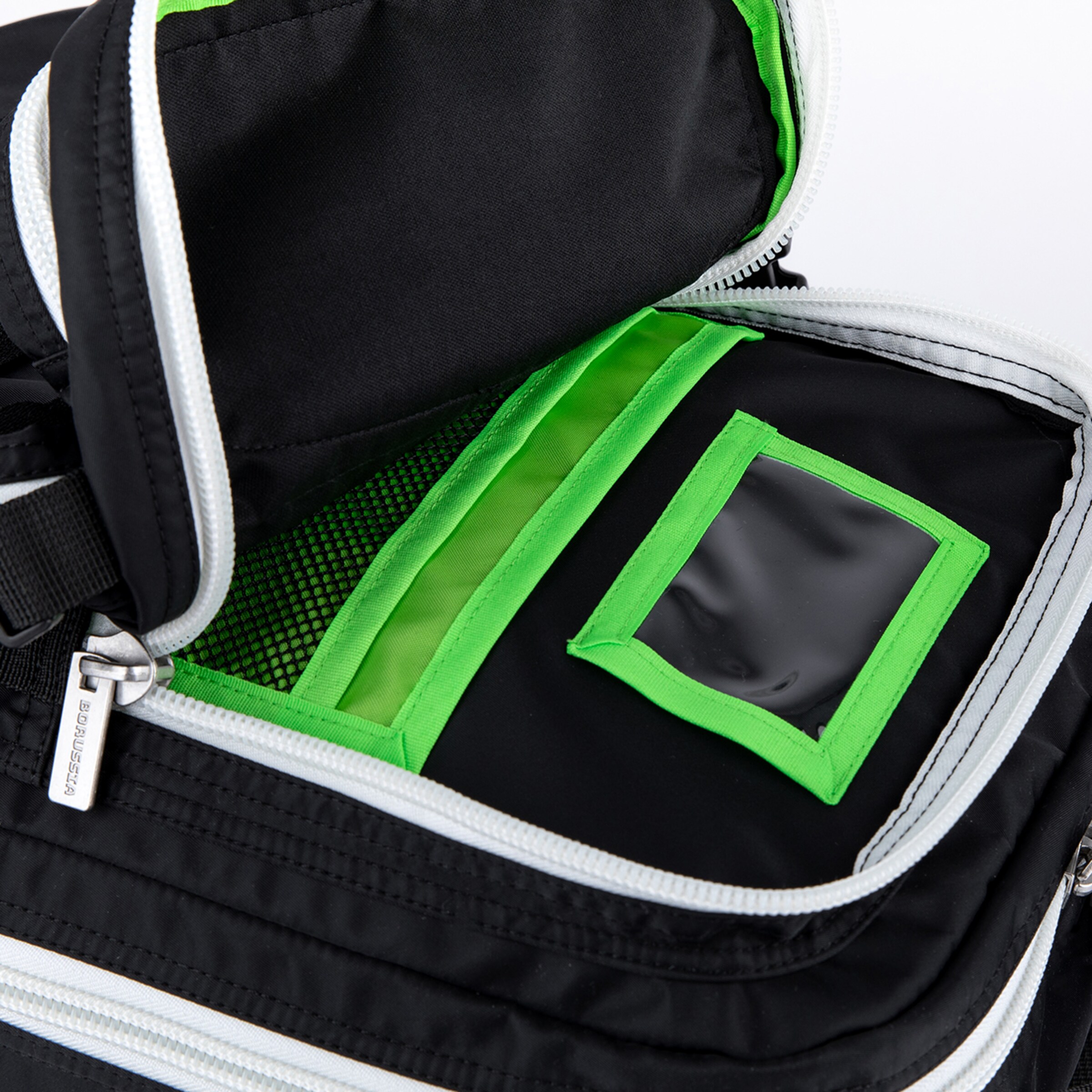Open black bag's main compartment with white zippers and green interior accents. Features organizer pockets: a clear window pocket and a mesh pocket. 'BORUSSIA' branded zipper pull visible.