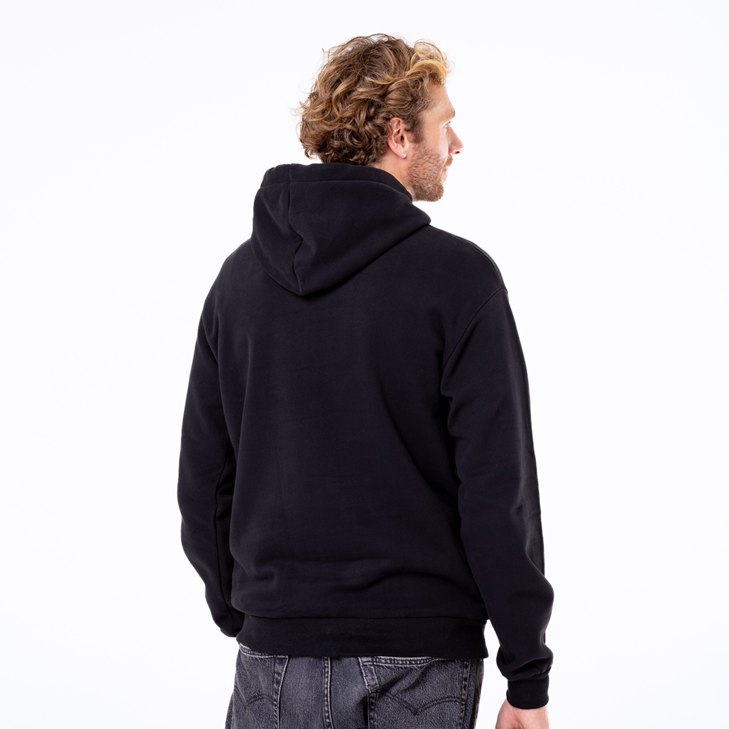 Mann mit lockigen Haaren trägt einen schwarzen Kapuzenpullover Rückenansicht.