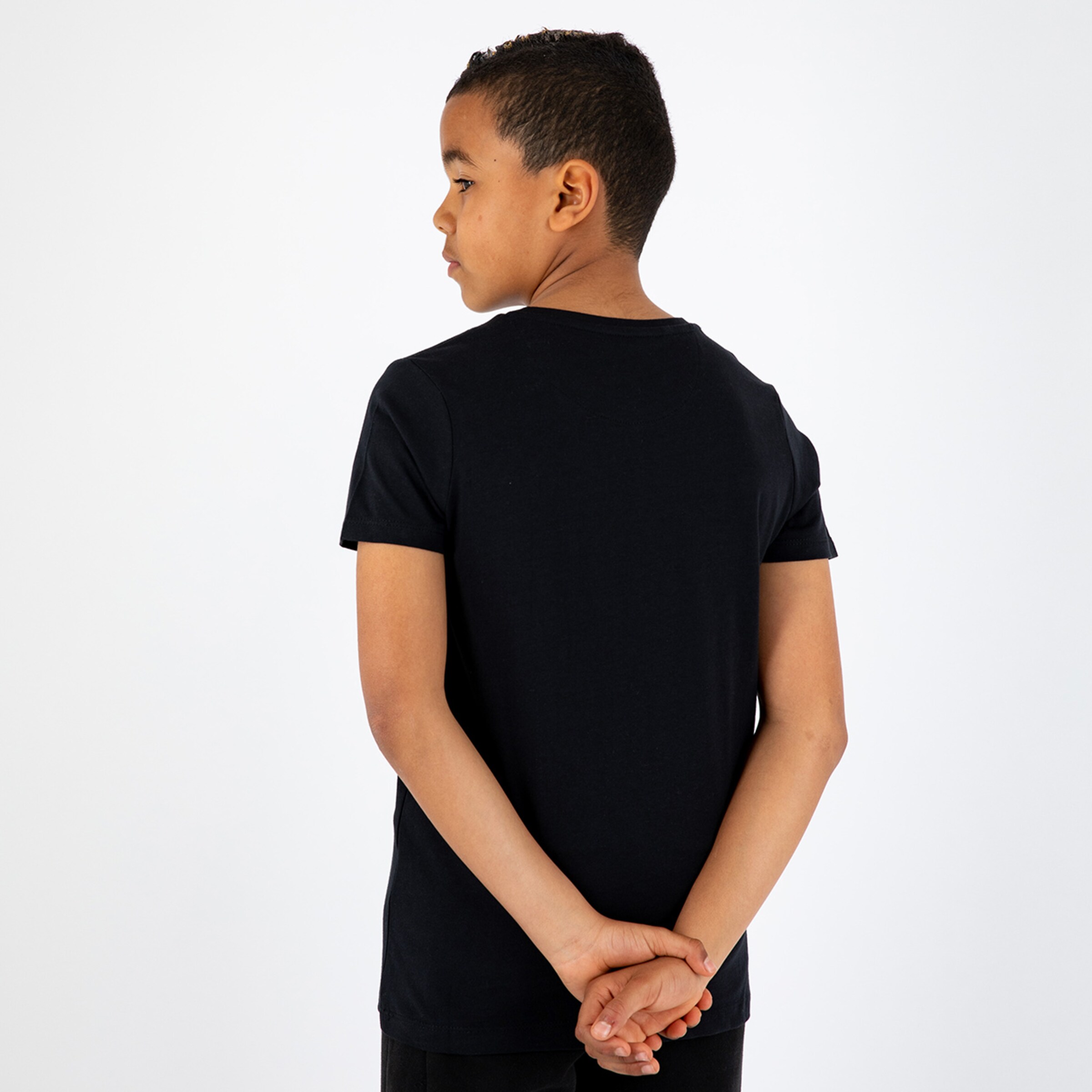 Ein Junge steht mit dem Rücken zur Kamera die Hände hinter dem Rücken verschränkt.