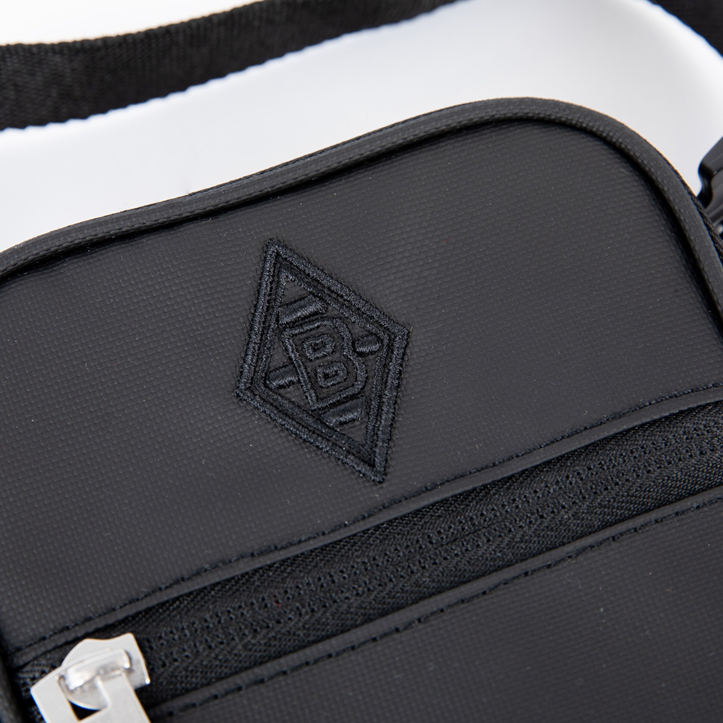 Nahaufnahme einer schwarzen Umhängetasche mit dem gestickten Logo von Borussia Mönchengladbach in Rautenform.