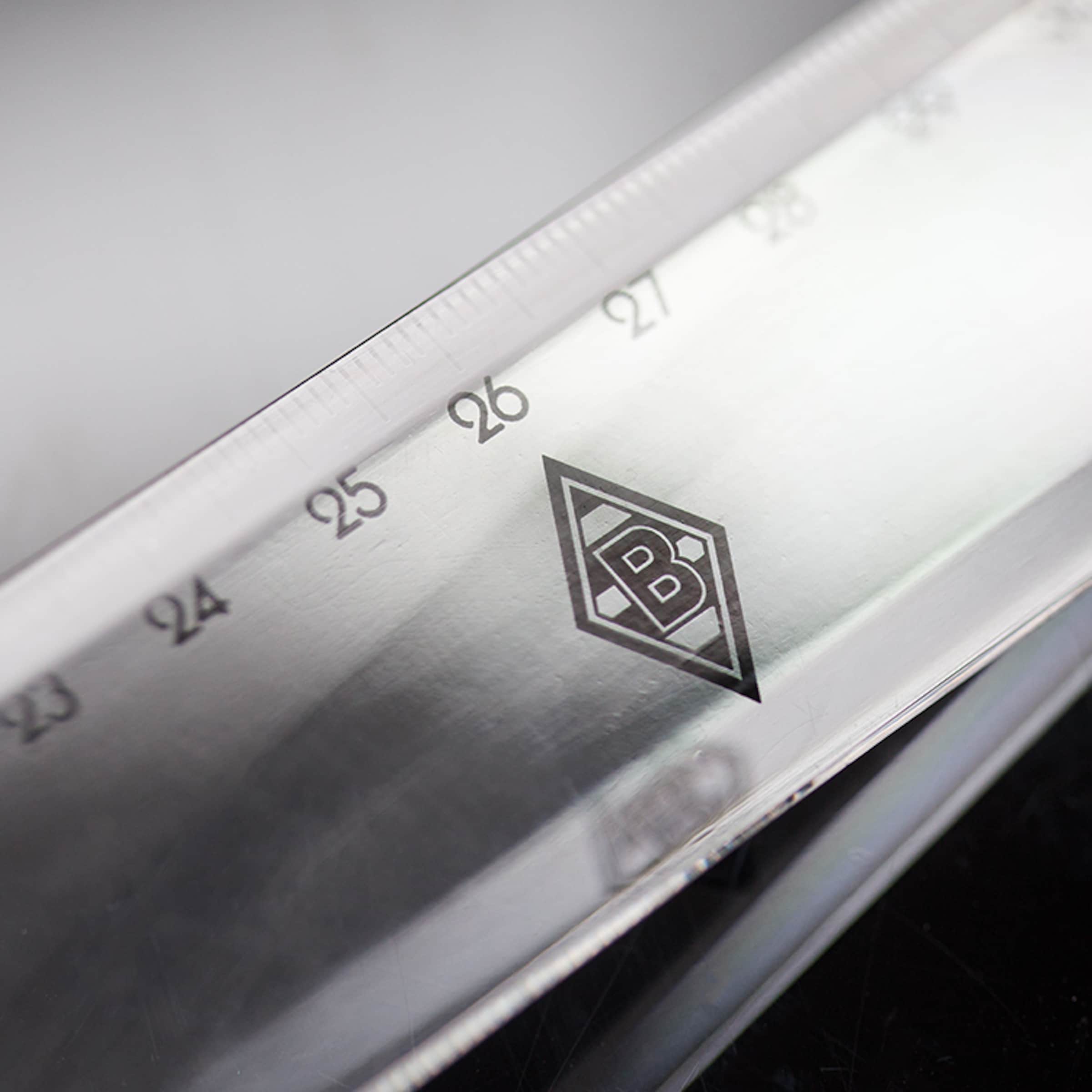 Nahaufnahme eines transparenten Lineals mit dem Borussia Mönchengladbach Logo zwischen den Markierungen 26 und 27.