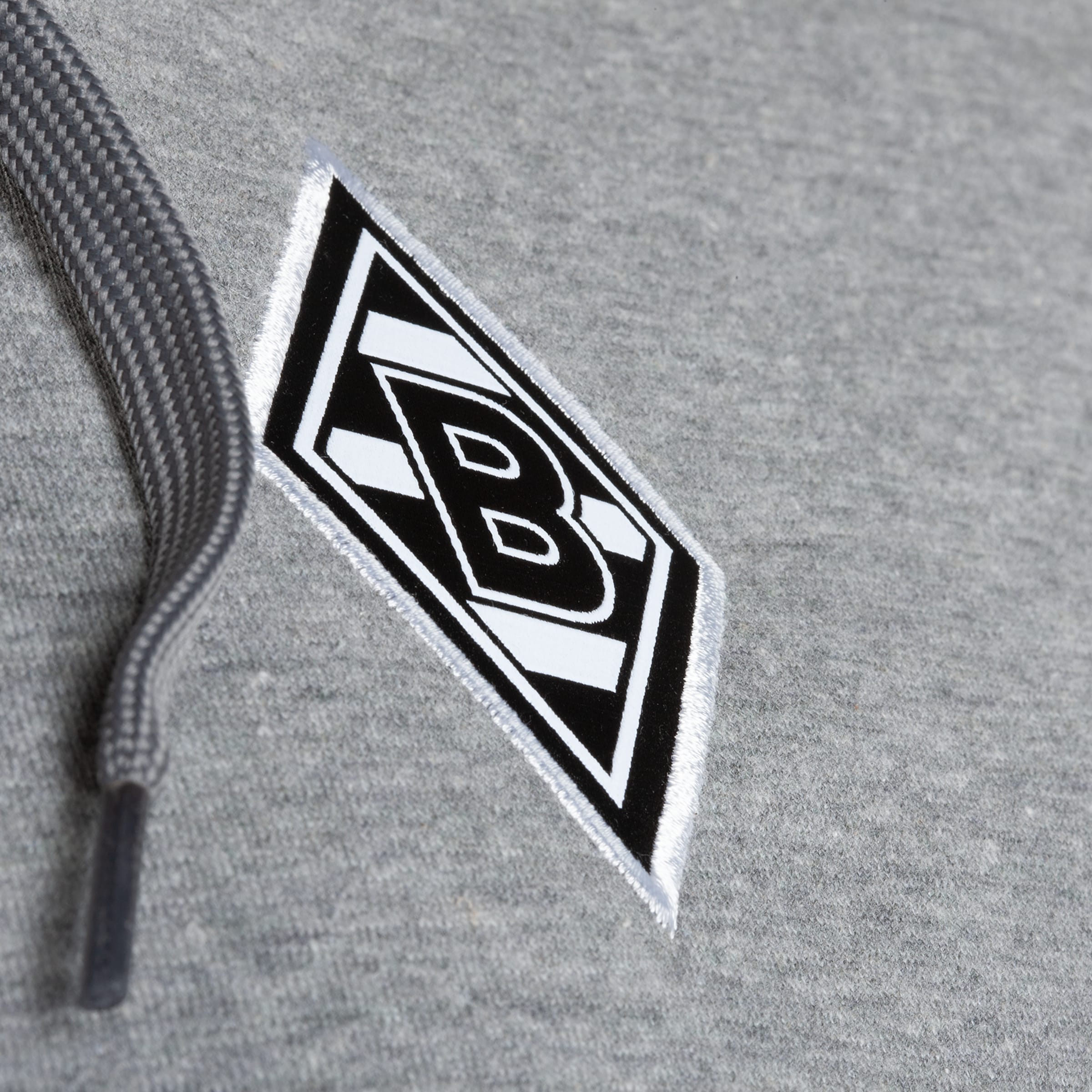 Nahaufnahme eines grauen Hoodies mit dem schwarz-weißen Logo-Patch von Borussia Mönchengladbach und einer grauen Kordel.