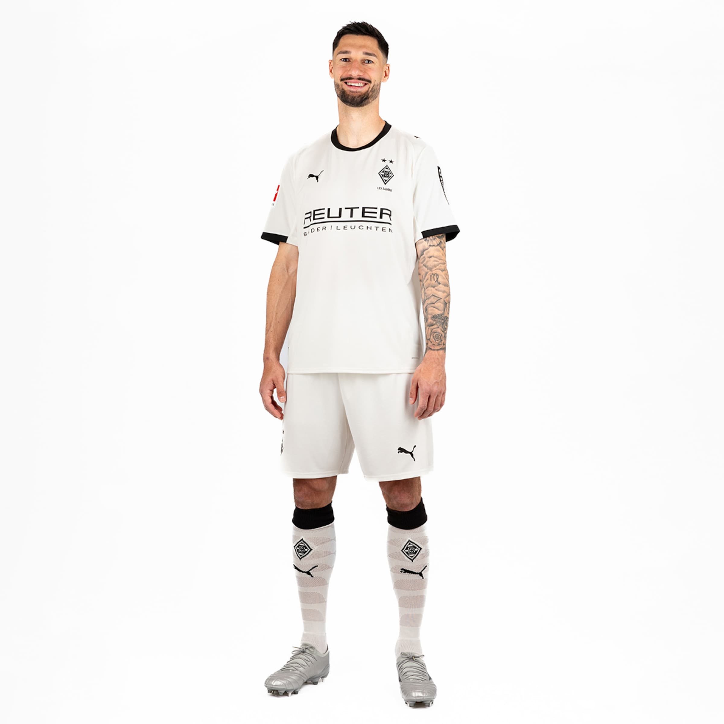 Spieler von Borussia Mönchengladbach in weißem Trikot und Shorts mit einem Lächeln.