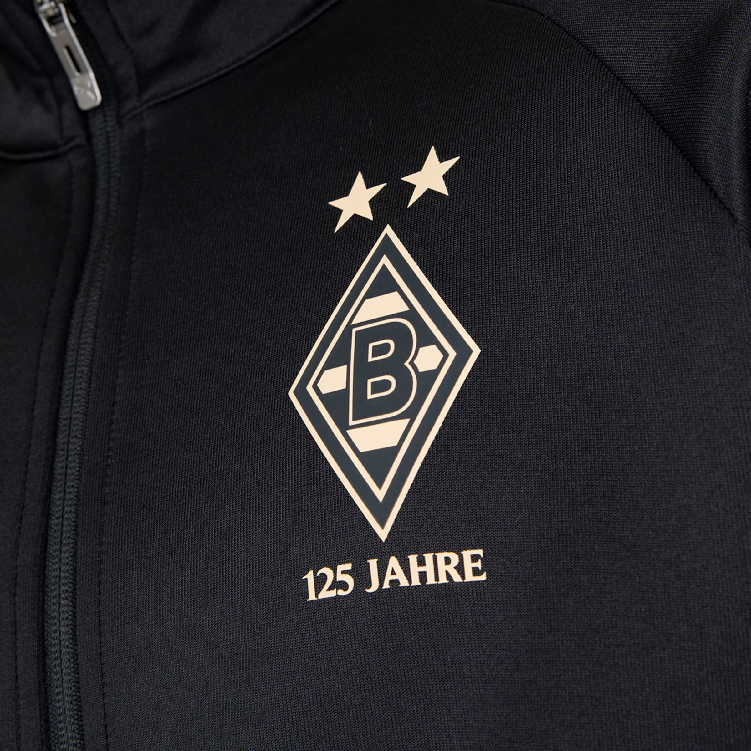Goldenes Borussia-Mönchengladbach-Wappen mit zwei Sternen und dem Schriftzug „125 JAHRE“ auf schwarzer Sportjacke.