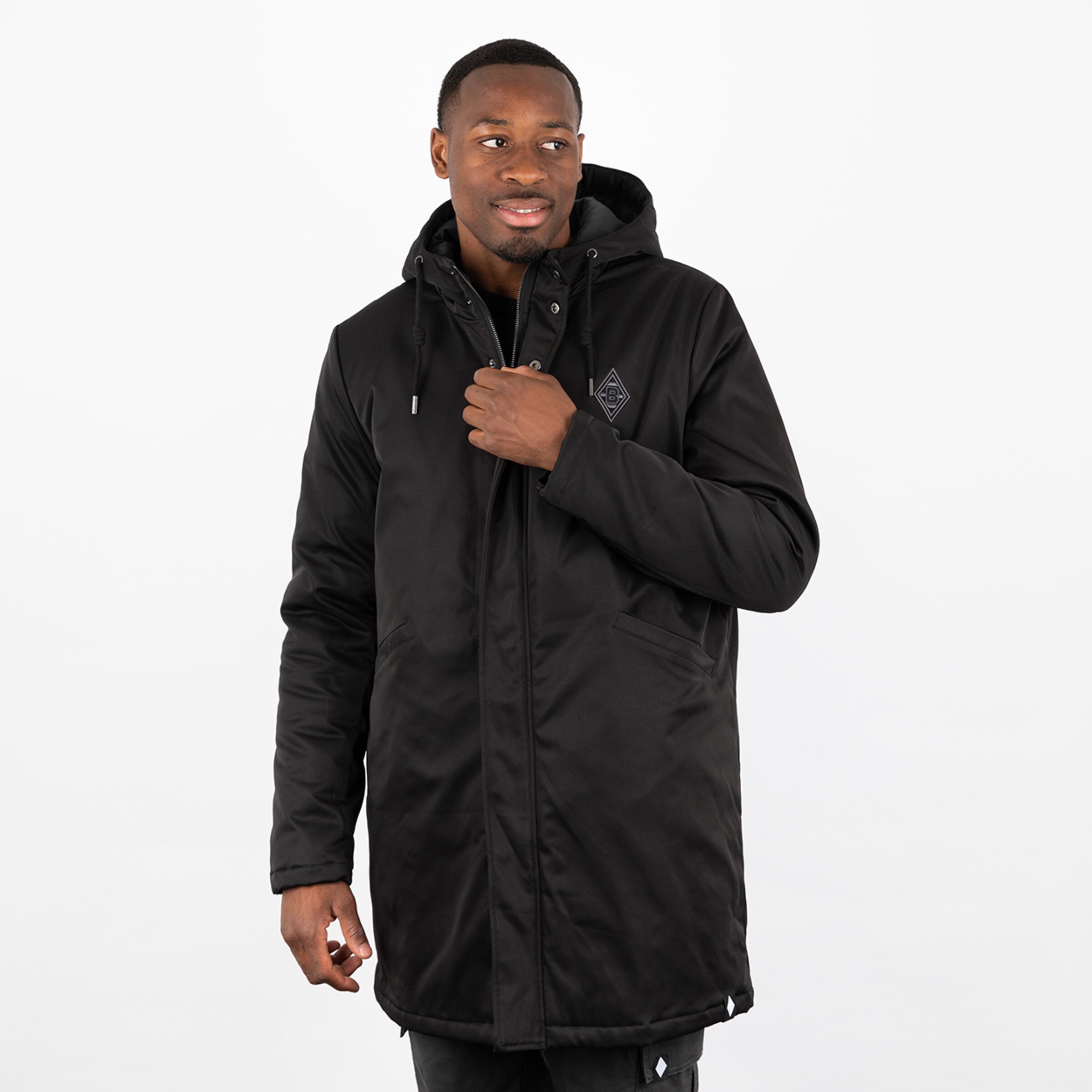 Junger Mann trägt einen langen schwarzen Parka mit Kapuze und lächelt.