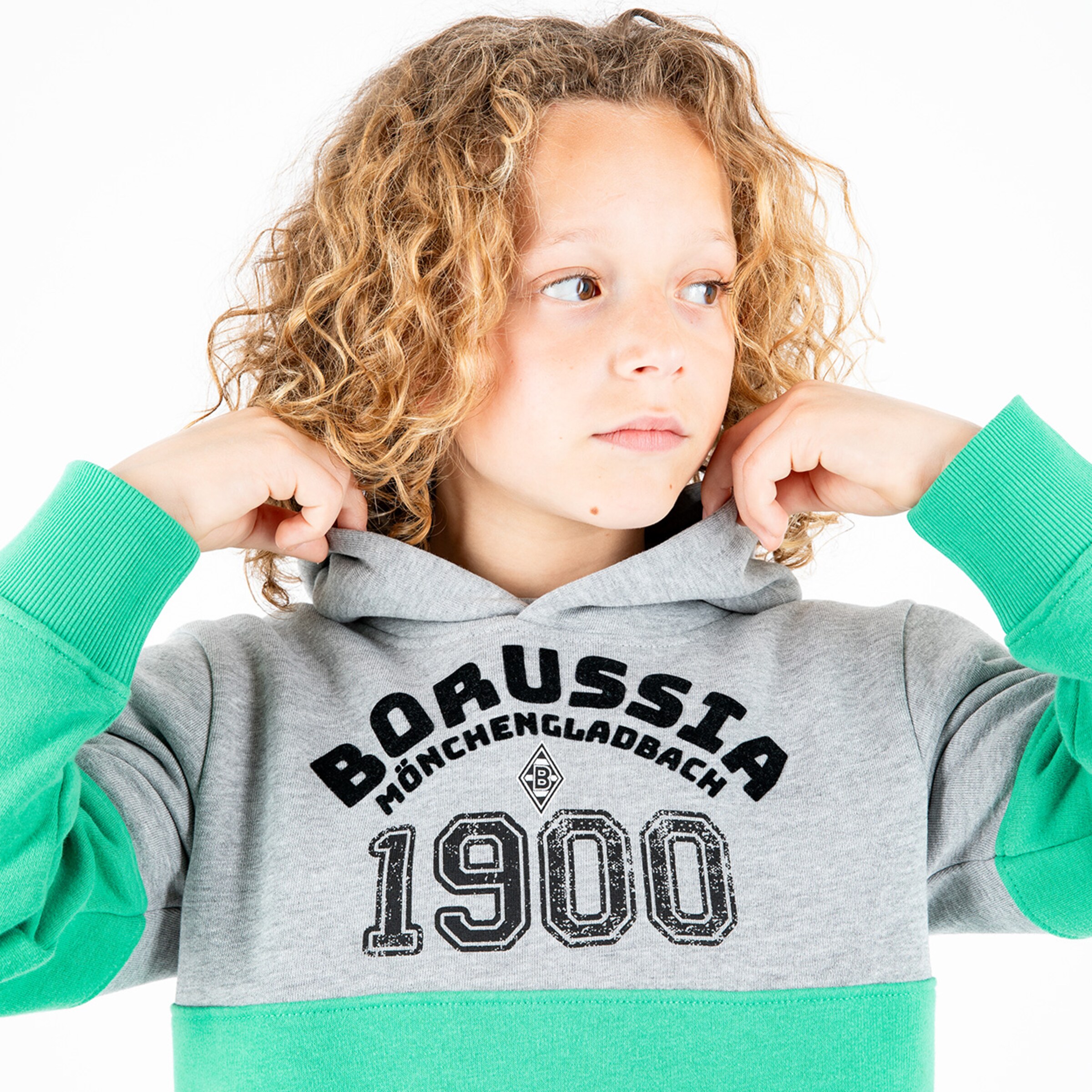 Ein Junge mit lockigen blondem Haar trägt einen grauen und grünen Pullover mit ‚Borussia Mönchengladbach 1900‘ Aufdruck.