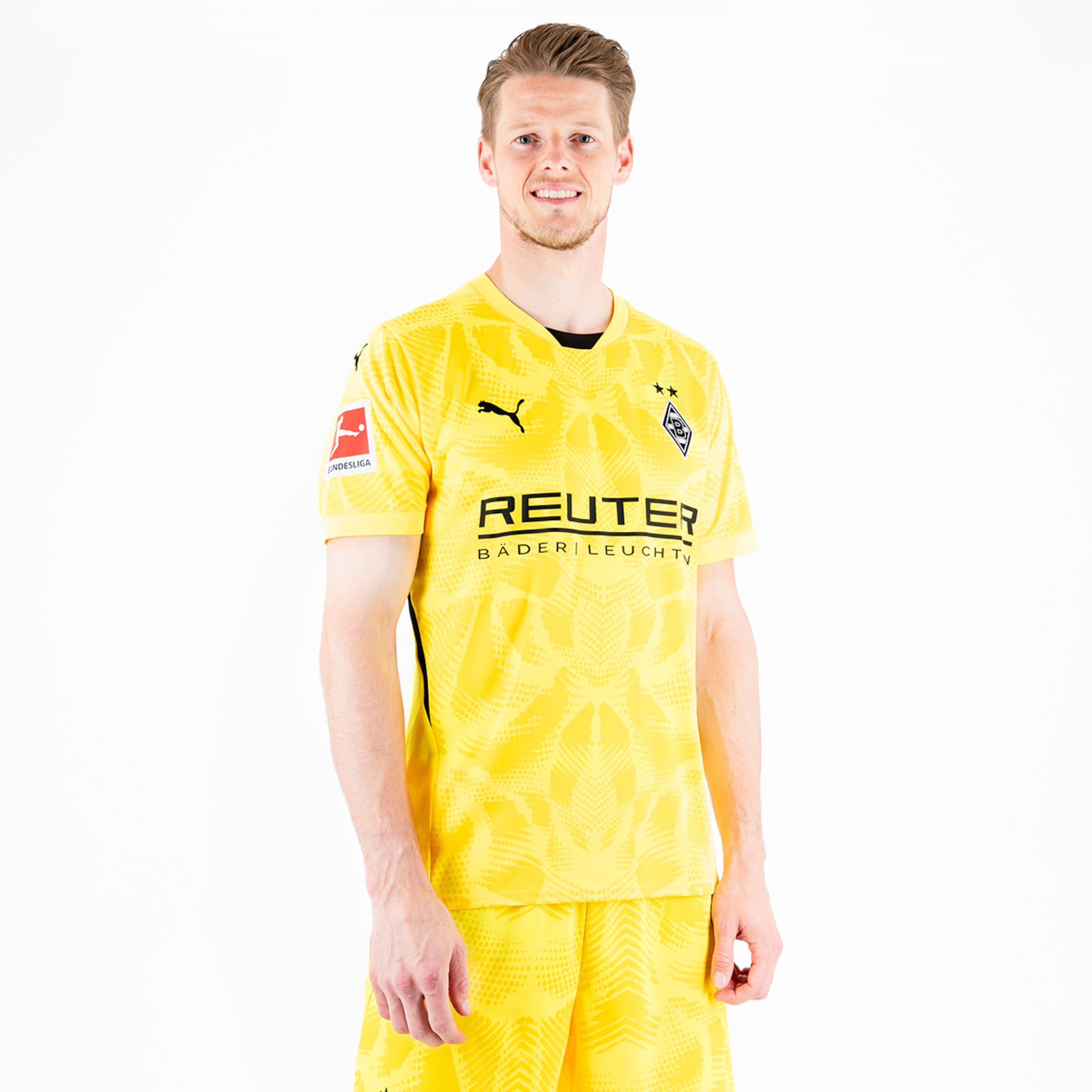 Torwart in gelbem Trikot mit dem Aufdruck REUTER BADERLEUCHT lächelt in die Kamera.
